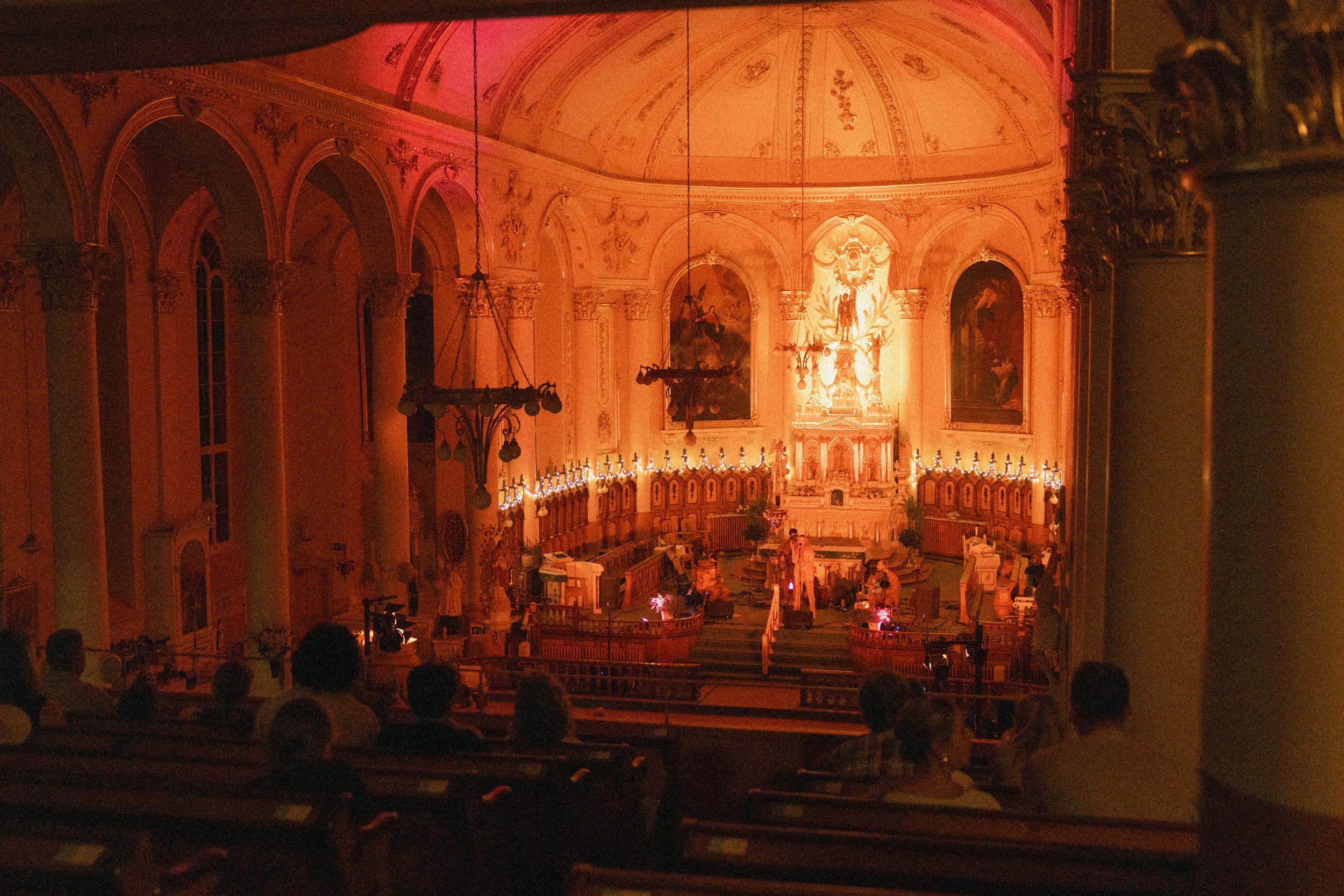 Intérieur d'une église ornée de dorures, peintures et sculptures, avec une lumière chaude et des personnes assises dans les gradins.