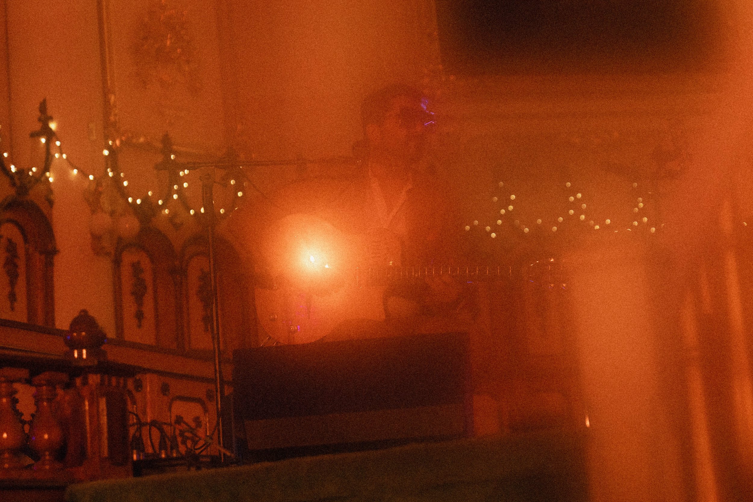 Une photo prise dans l'obscurité avec une forte teinte orange, montrant un bâtiment avec des décorations en fil lumineux et un ciel chargé de fumée ou de brume, probablement à cause d'un événement ou d'un incendie.