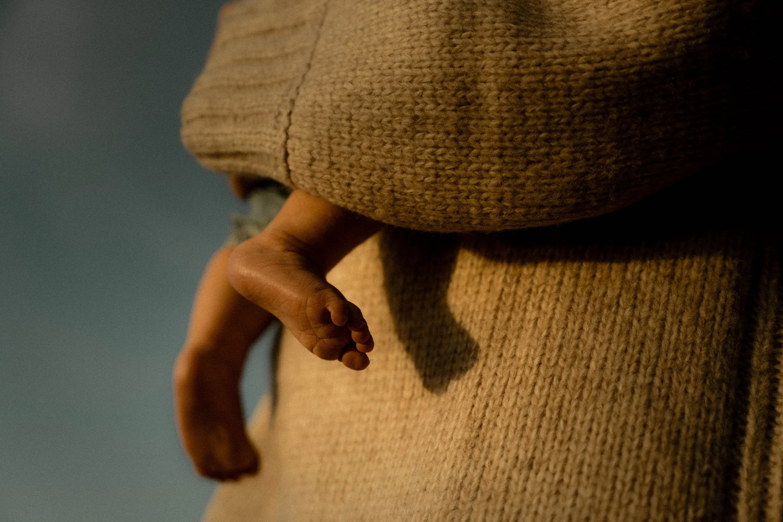 Main d'enfant tenant la main d'une femme sur un vêtement en tricot beige, avec un fond de ciel clair.