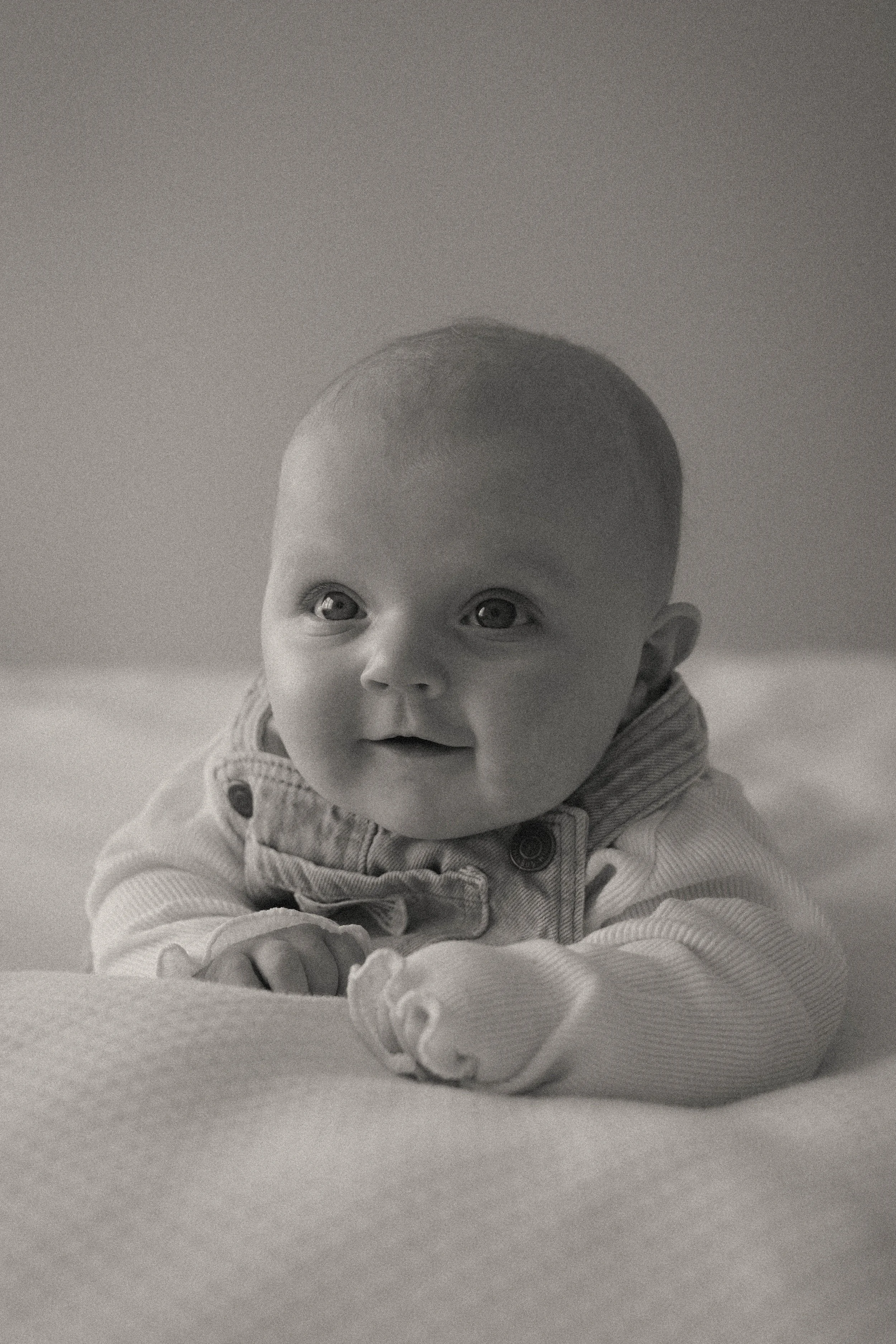 Un bébé regarde vers le haut avec une expression curieuse, vêtu d'une veste à rayures, posé sur une surface plane, en noir et blanc.