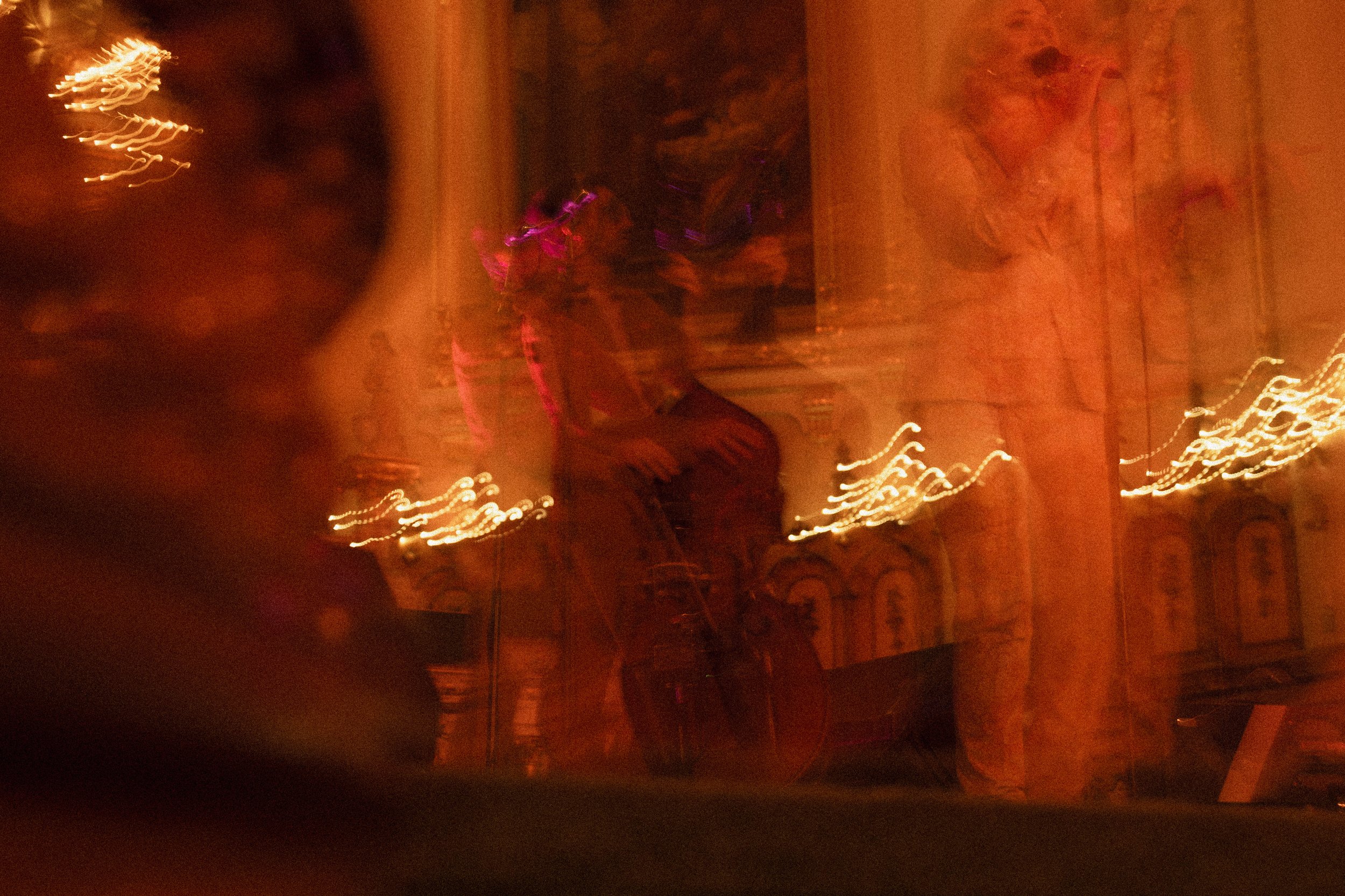 Image floue et sombre avec des lumières scintillantes, peut-être une scène de fête ou de spectacle dans une salle avec des murs en pierre.
