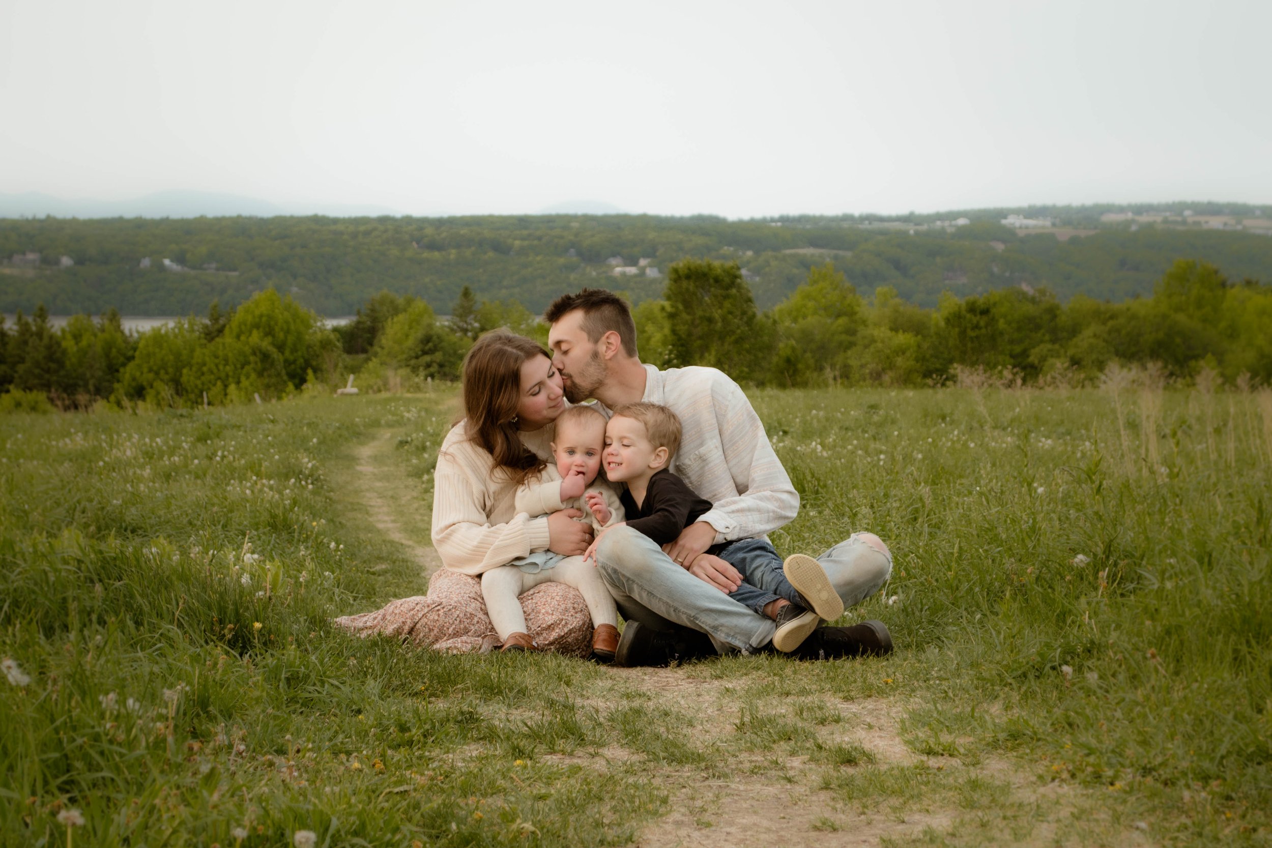 Une famille faisant une photo dans un champ verdoyant avec des arbres et une vue sur des collines au loin.
