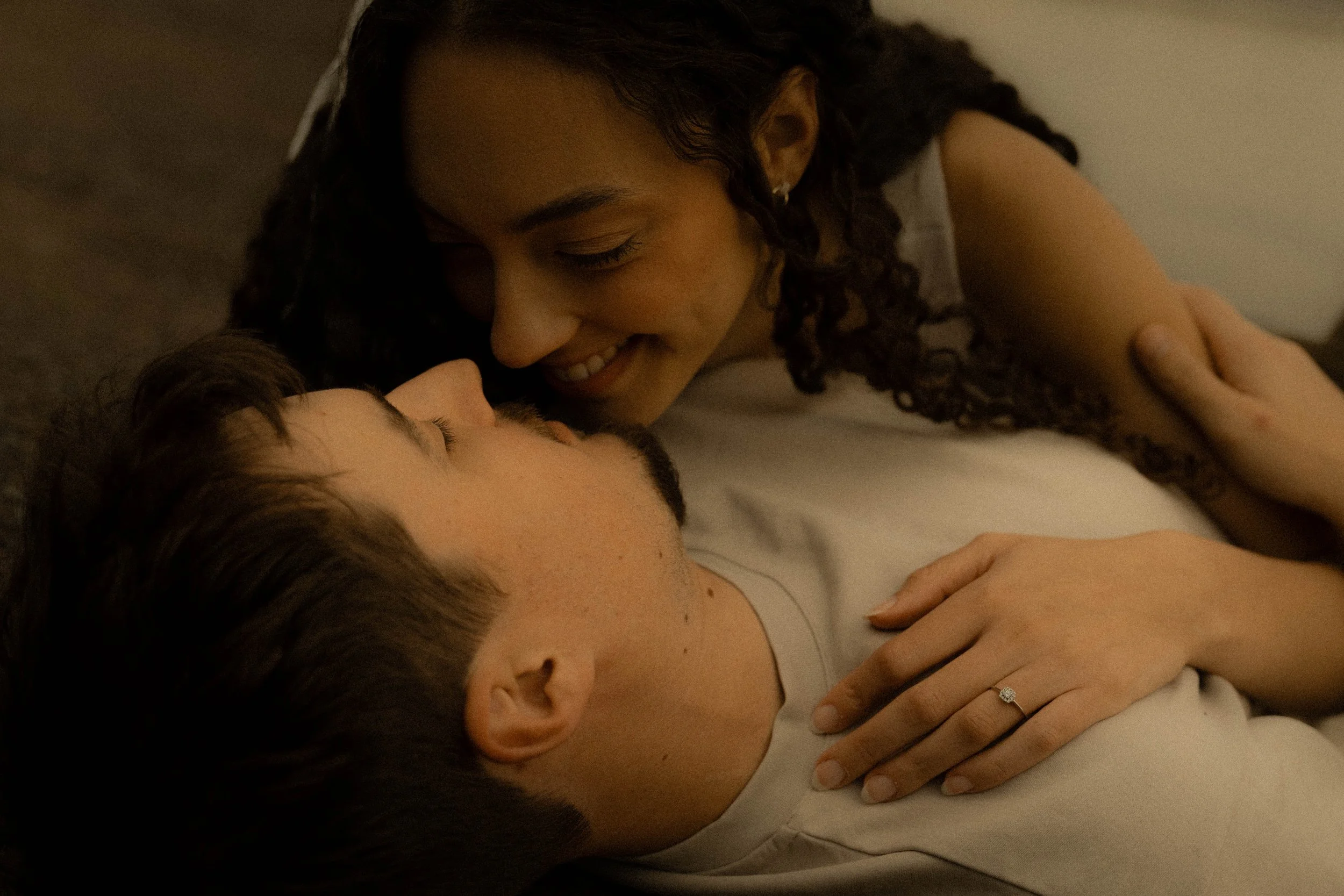 Une femme avec des cheveux bouclés et un homme ayant les yeux fermés, tous deux allongés, exprimant de la tendresse et de l'intimité, dans une scène douce et chaleureuse.