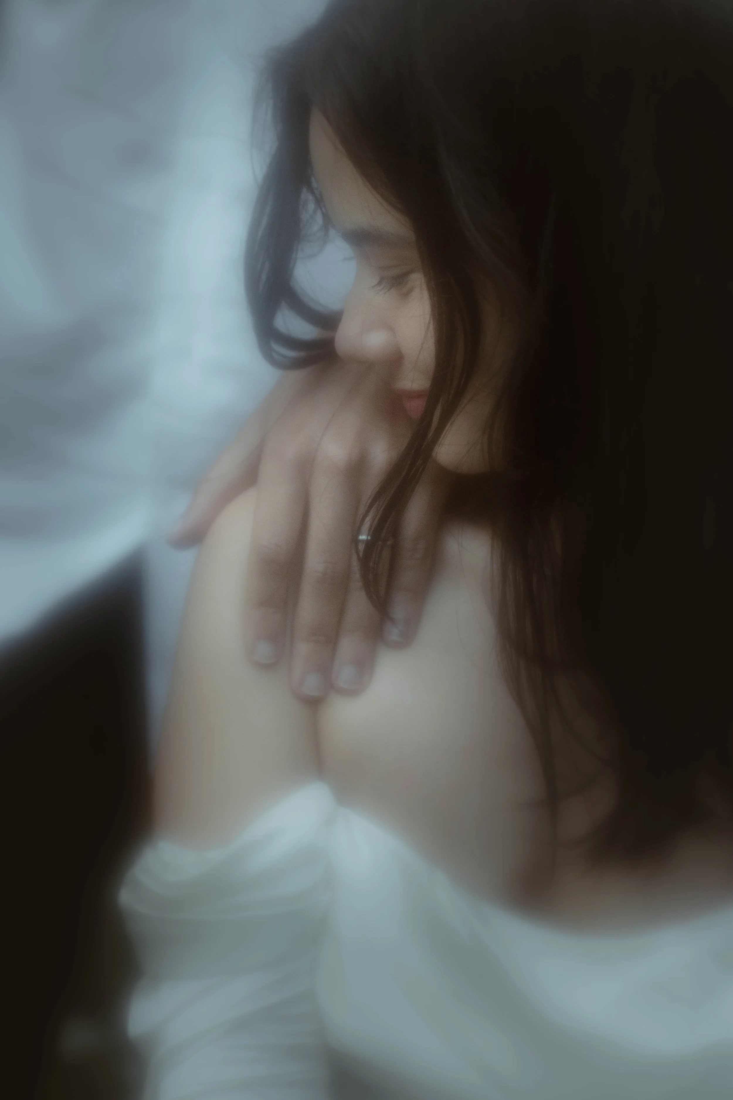 Une femme aux cheveux longs, foncés, de profil, dont le visage est face à la main de quelqu'un d'autre. La scène dégage une atmosphère intime et douce.
