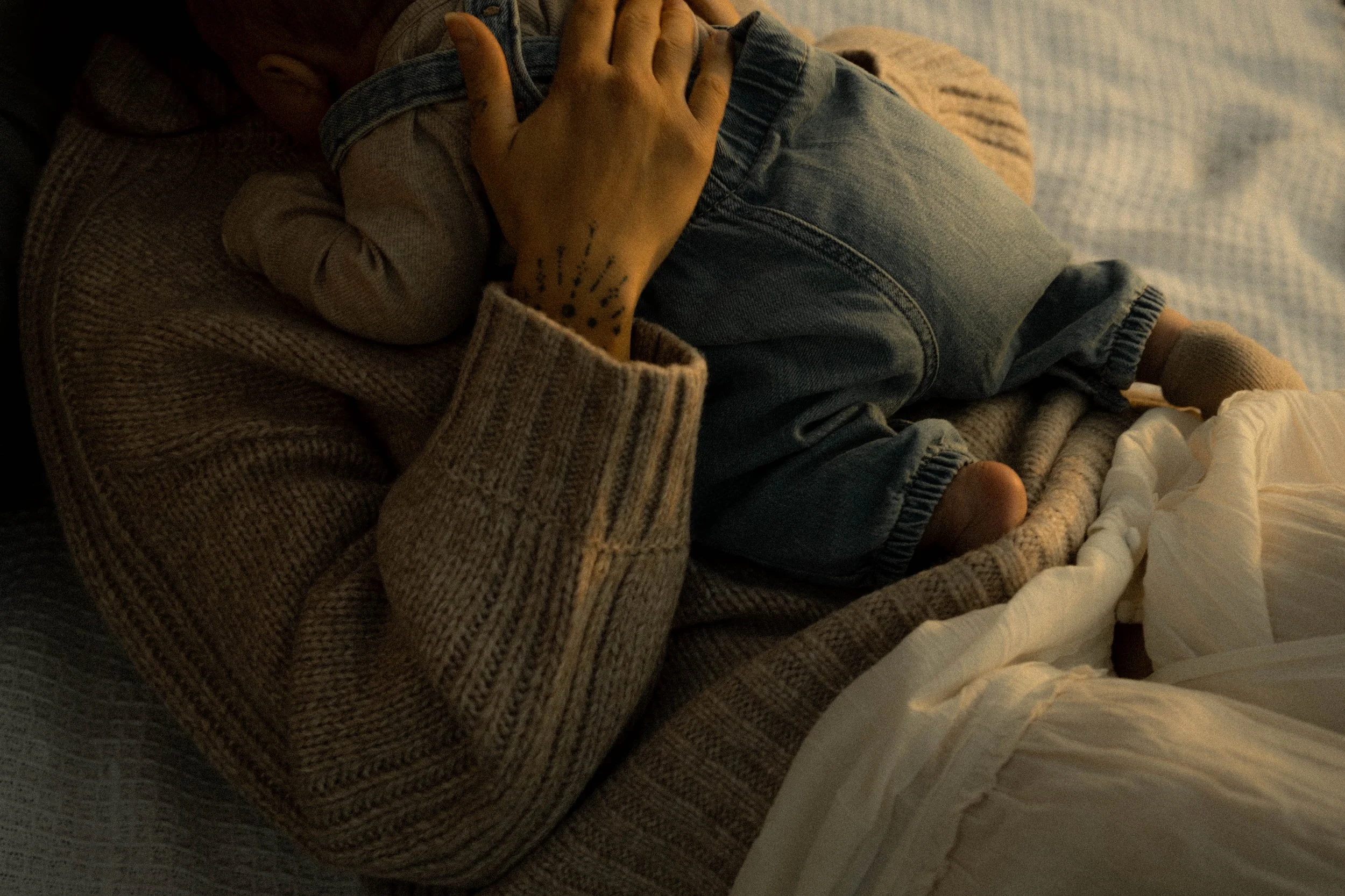Personne qui serre dans ses bras un bébé, tous deux allongés sur un lit, dans un éclairage tamisé.