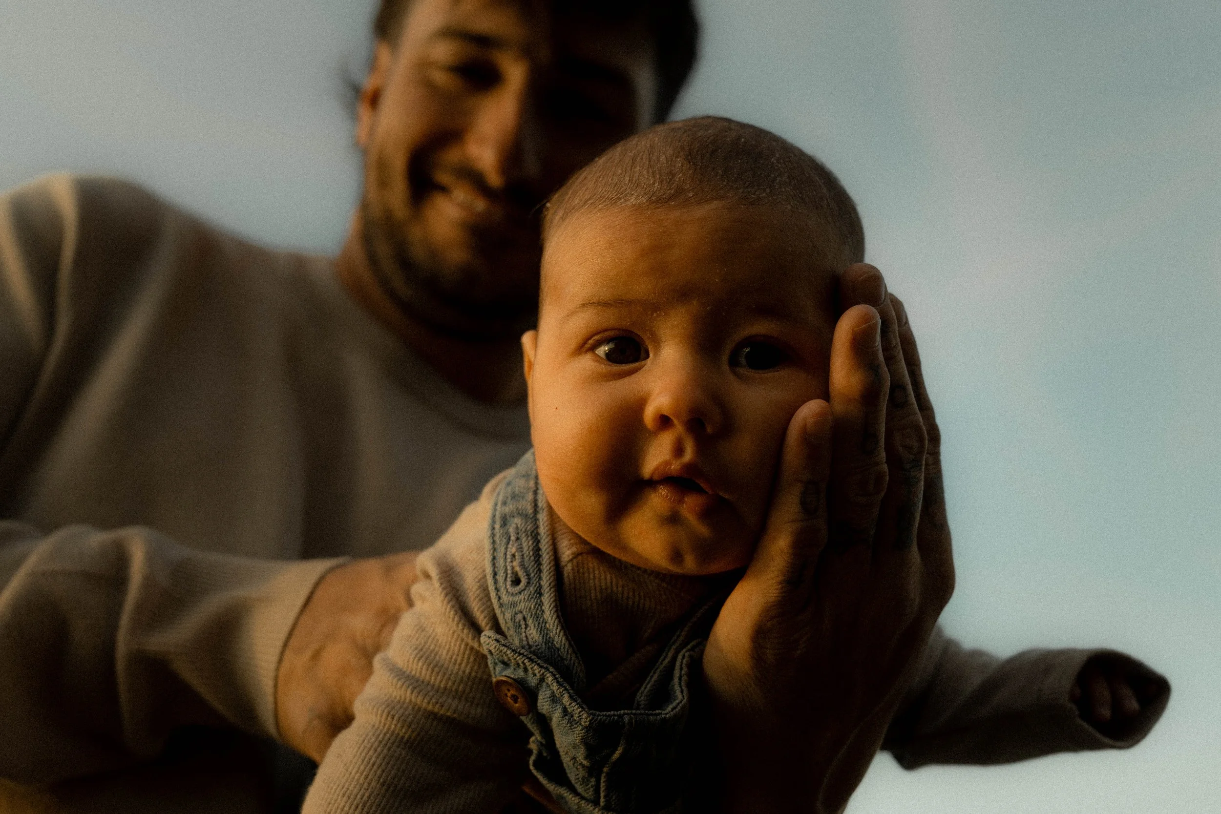 Un homme et un jeune garçon regardant la caméra, avec l'homme tenant le garçon par le visage. L'il est en gros plan, et il regarde directement vers l'objectif.
