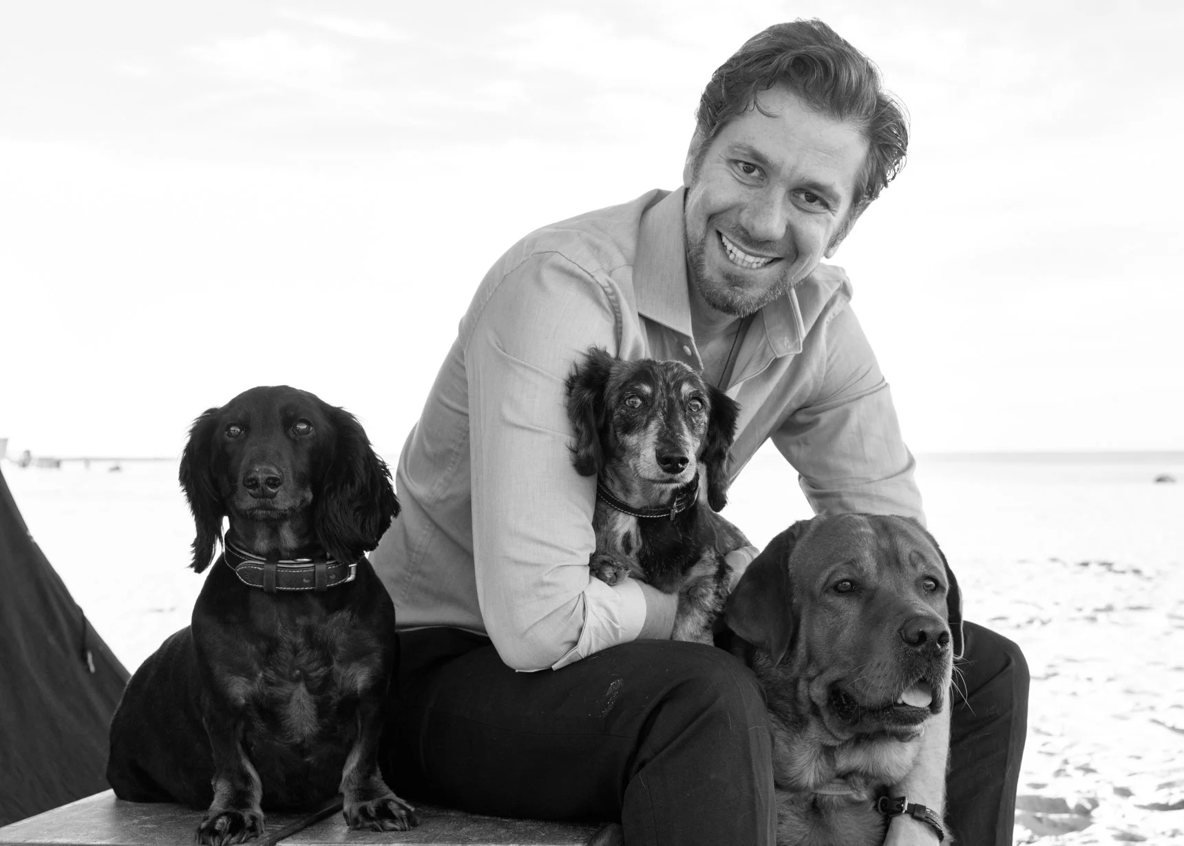 A smiling man with three dogs on a beach