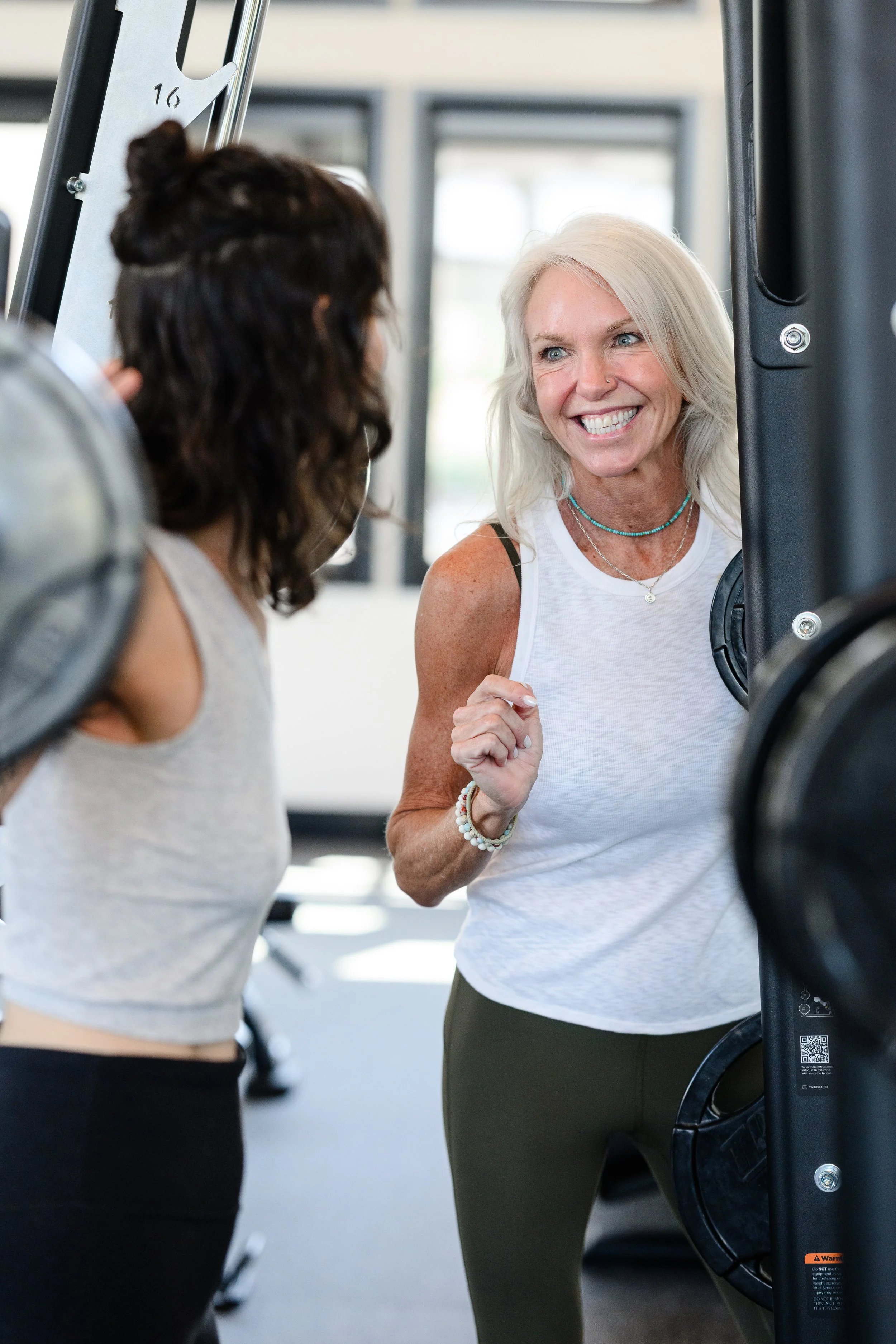 A smiling female personal trainer helping a client with her form while lifting weights