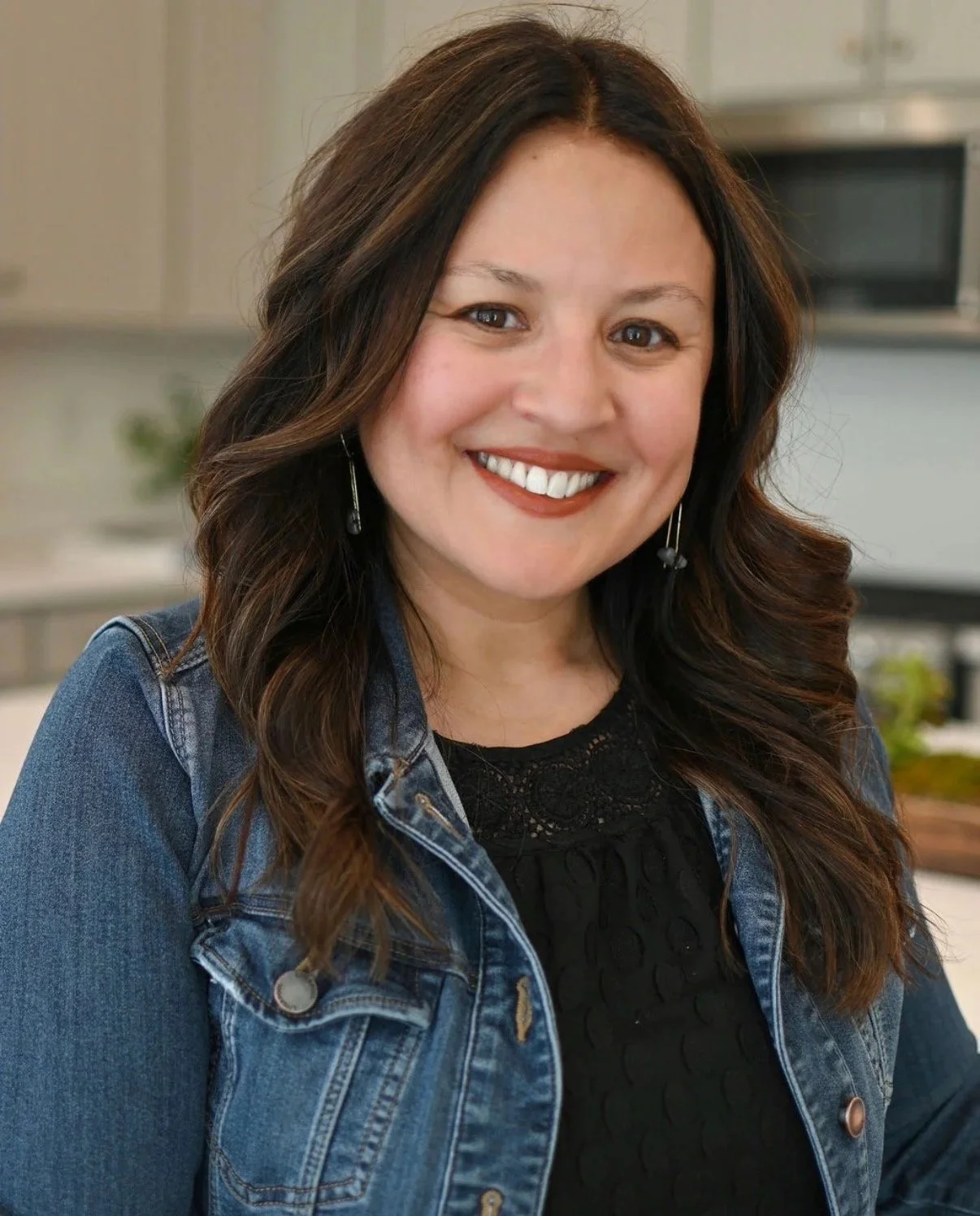 A woman with red hair and tattoos on her arm uses a laptop on her lap, sitting on a teal couch with a white pillow with green and black lines in a living room.