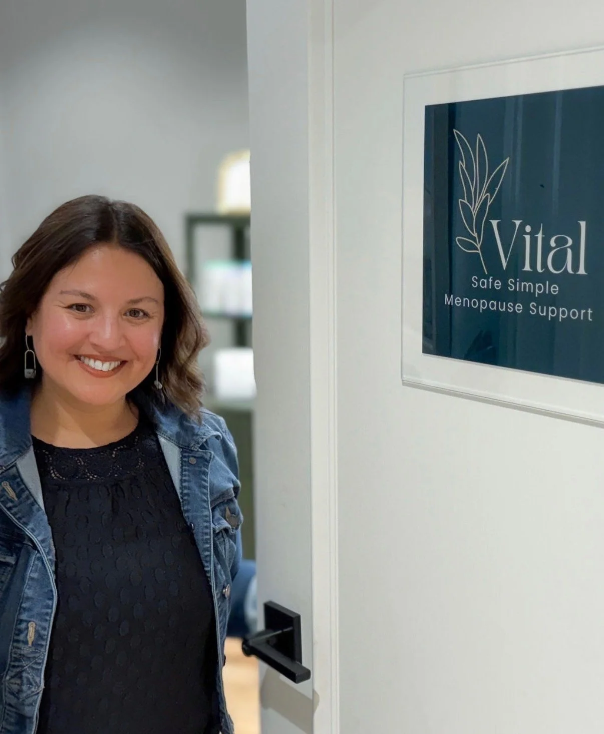 A woman smiling standing next to a sign that says 'Vital - Safe Simple Menopause Support'.