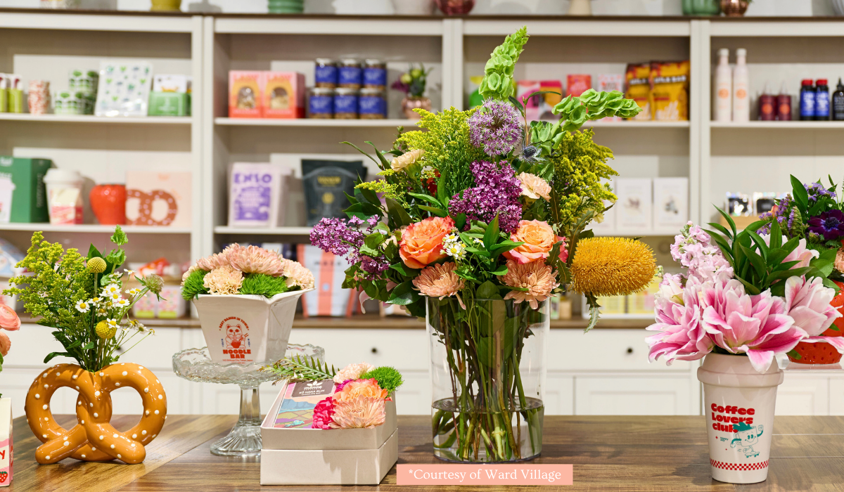 Colorful flower arrangements in vases and pots on a wooden table in a shop. Background shelves display various products.