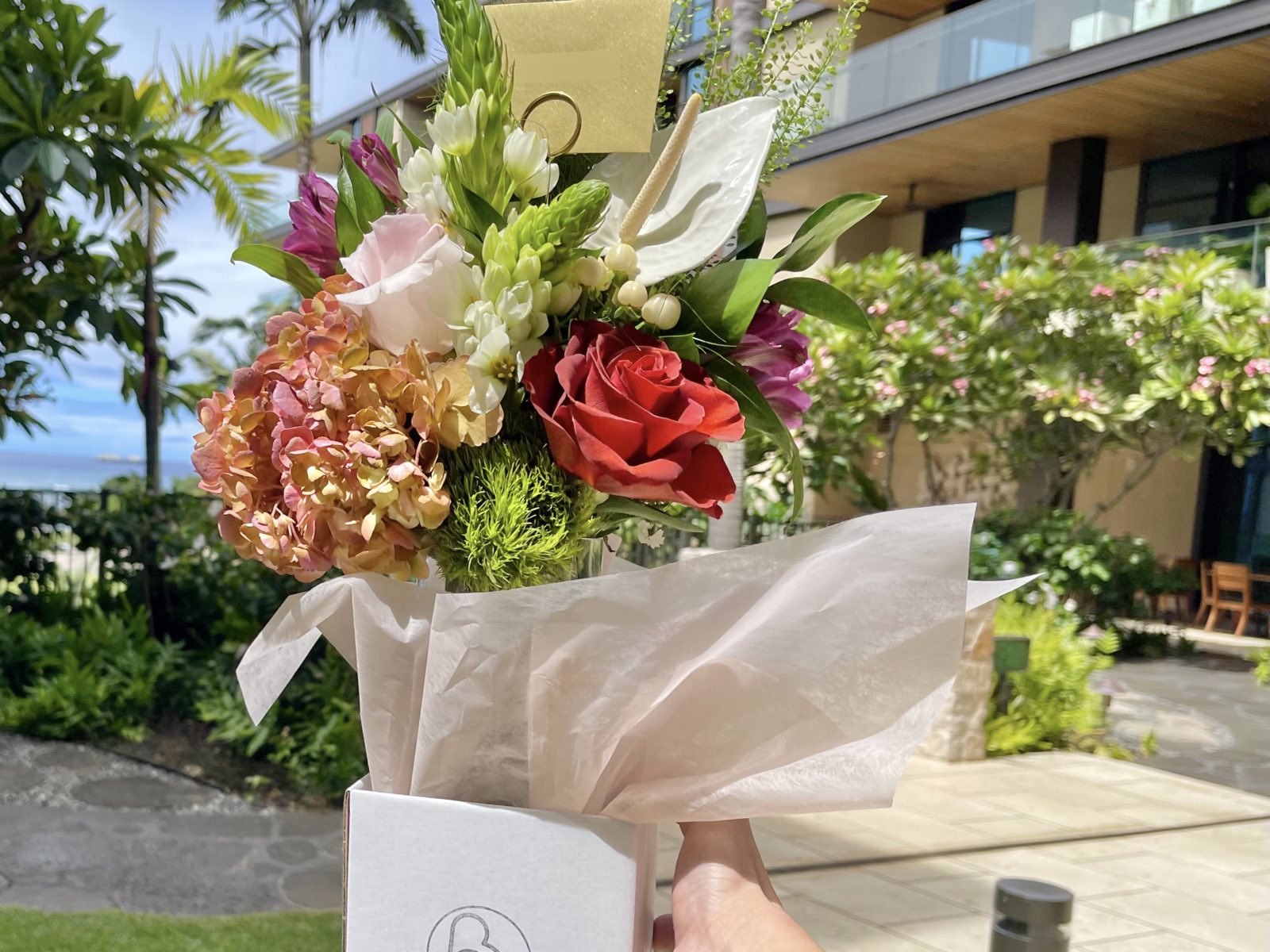 Luxury hand-tied flower arrangement with red rose, hydrangea, anthurium, and tropical blooms in elegant white packaging, delivered to an upscale O‘ahu resort for premium same-day flower delivery in Honolulu, Hawaii.