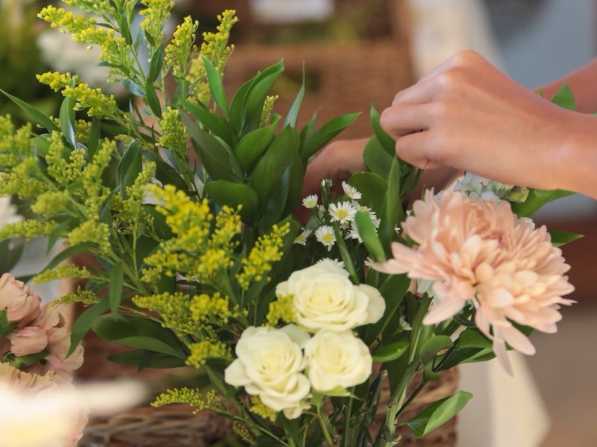 Person arranging a bouquet of mixed flowers, including white roses, peach dahlias, yellow solidago, and small white daisies.