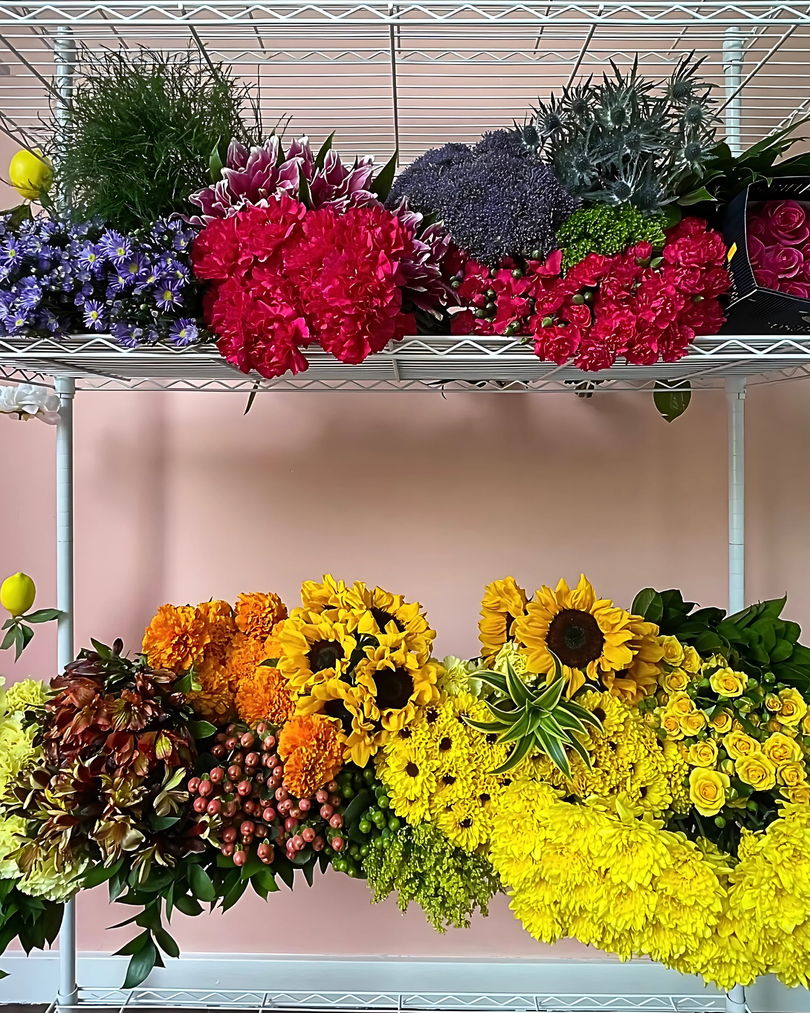 Colorful flower arrangements on metal shelving units, including pink, purple, orange, yellow, and green flowers.