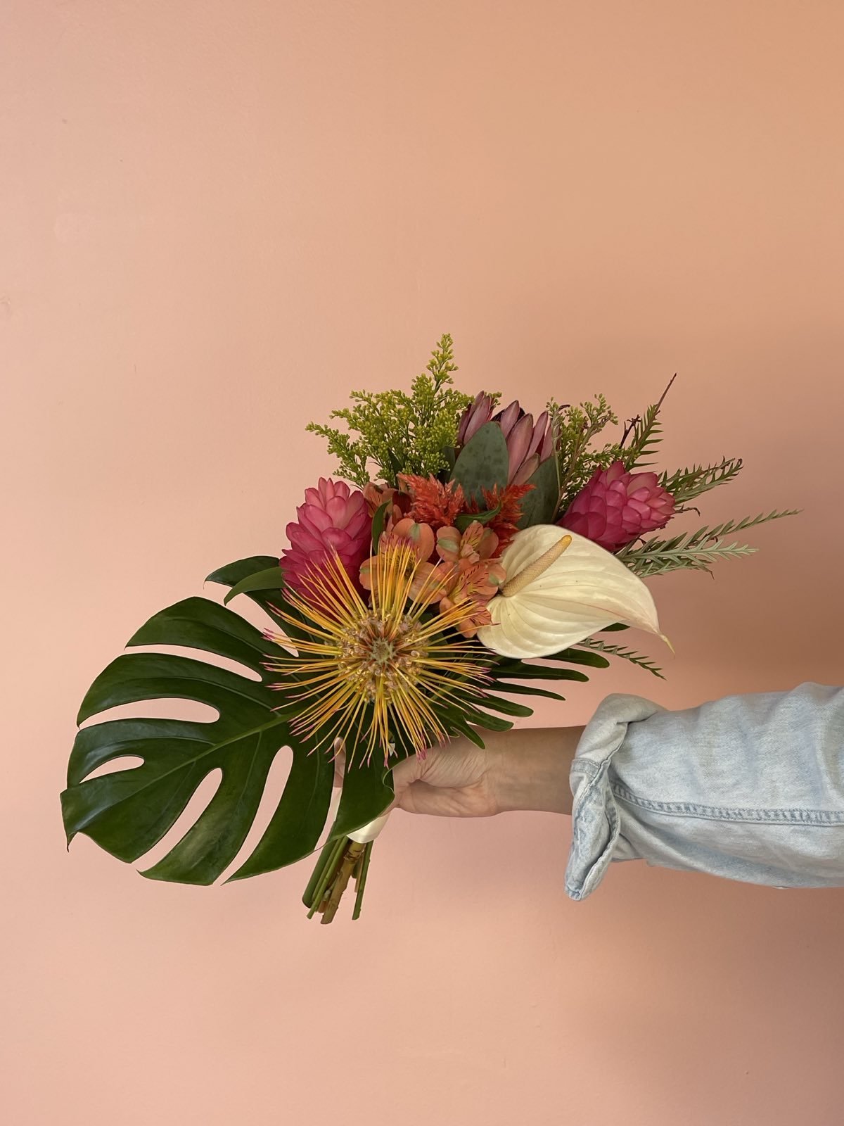 Person holding a colorful tropical flower bouquet against a pink background.