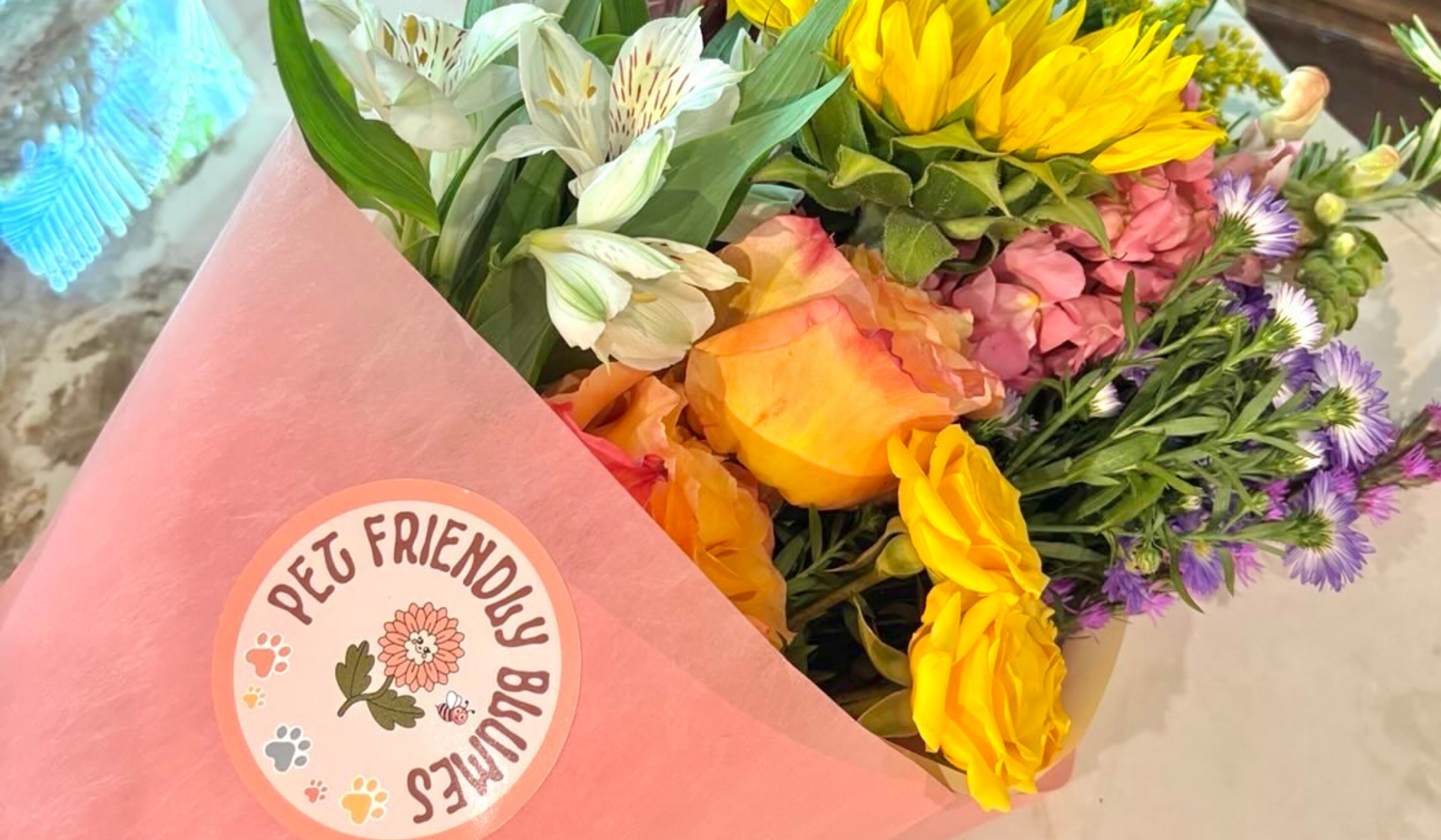 Colorful bouquet of various flowers wrapped in pink paper with a sticker that says "Pet Friendly" and has a flower and paw print designs.