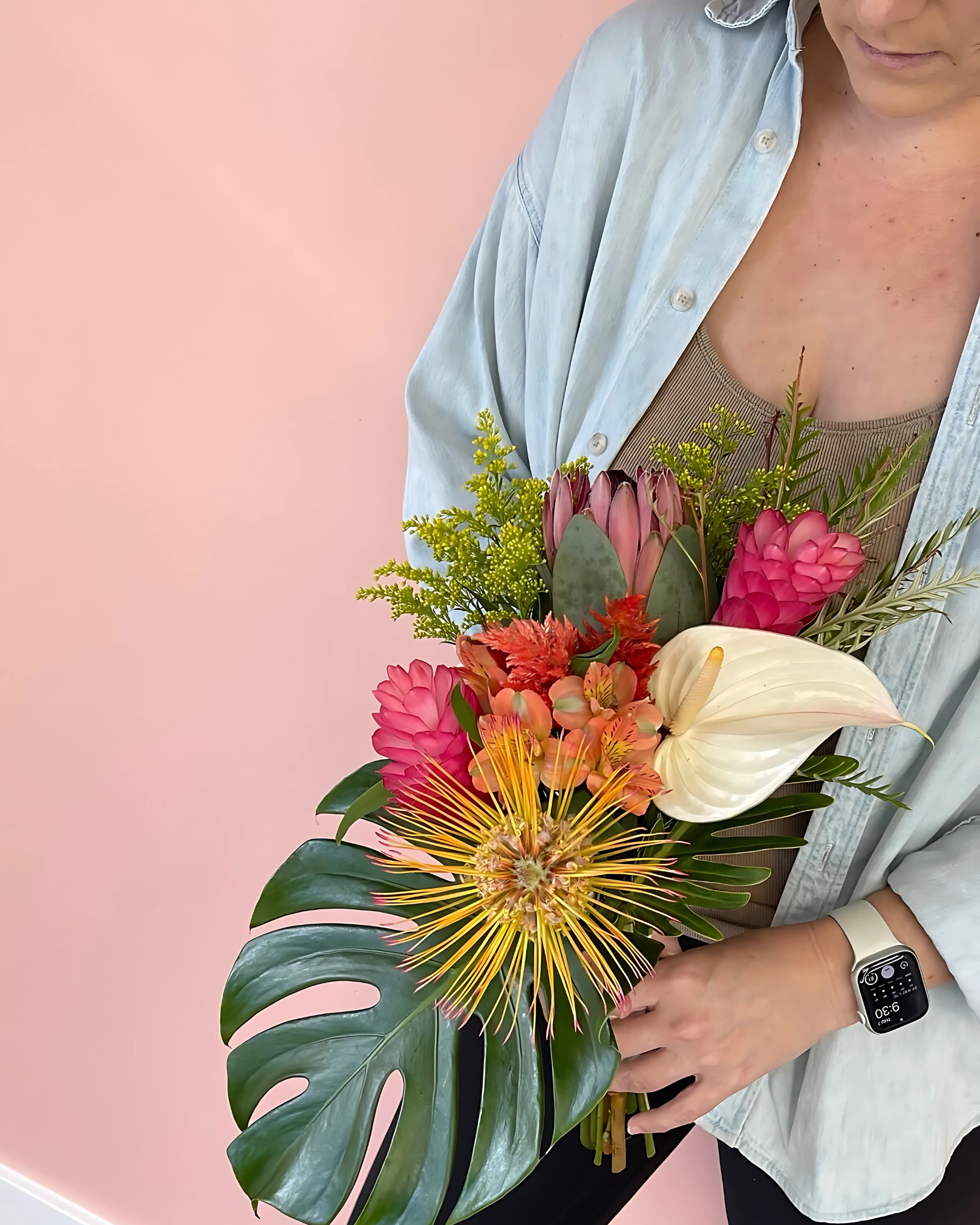 Person holding a colorful bouquet of tropical flowers with a pink background