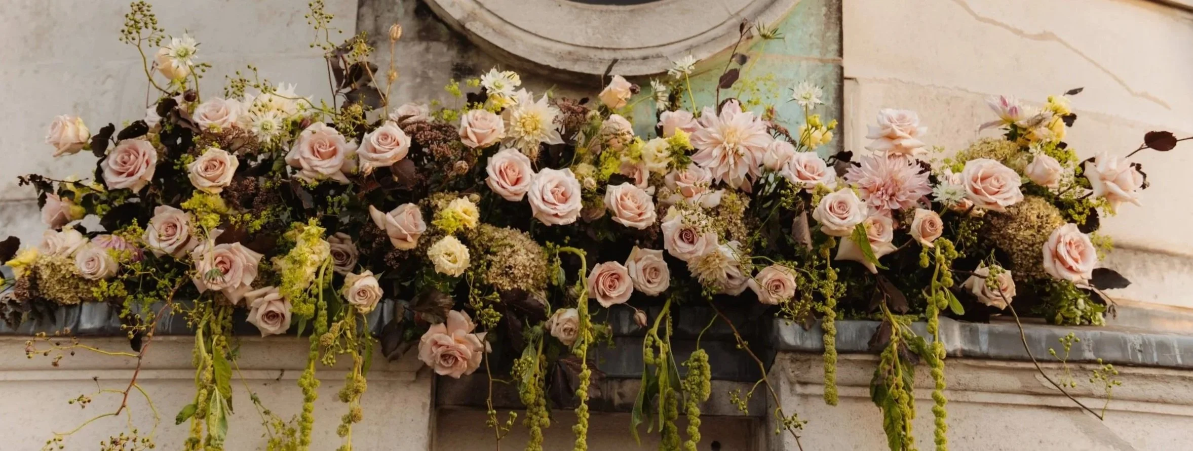 Garden-inspired wedding floral installation with blush and cream flowers and natural greenery.