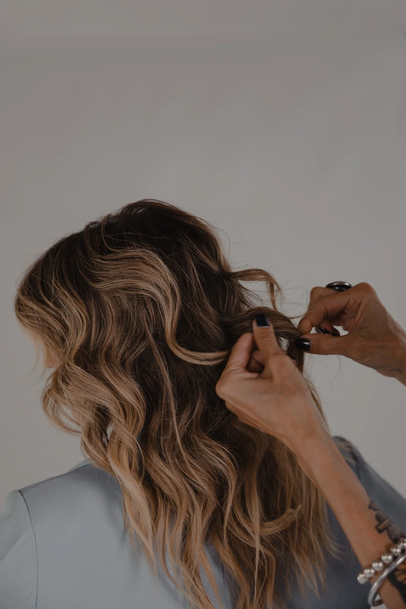 Hands styling wavy highlighted hair on a client from behind