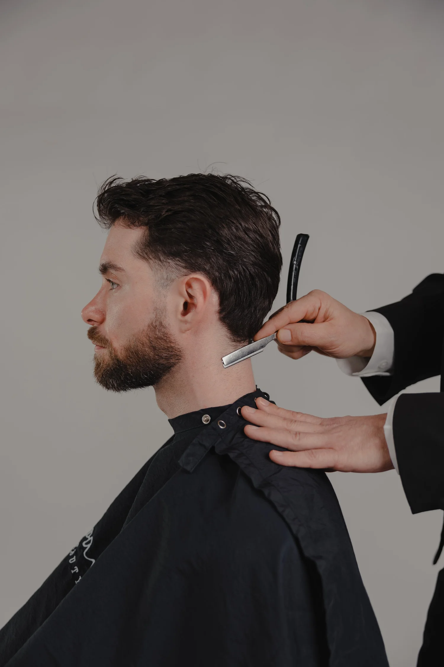 Barber using a razor on a man's neckline with a cape on