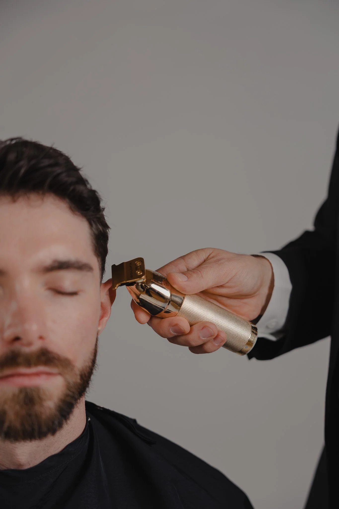 Barber using a gold trimmer on a bearded man's sideburn