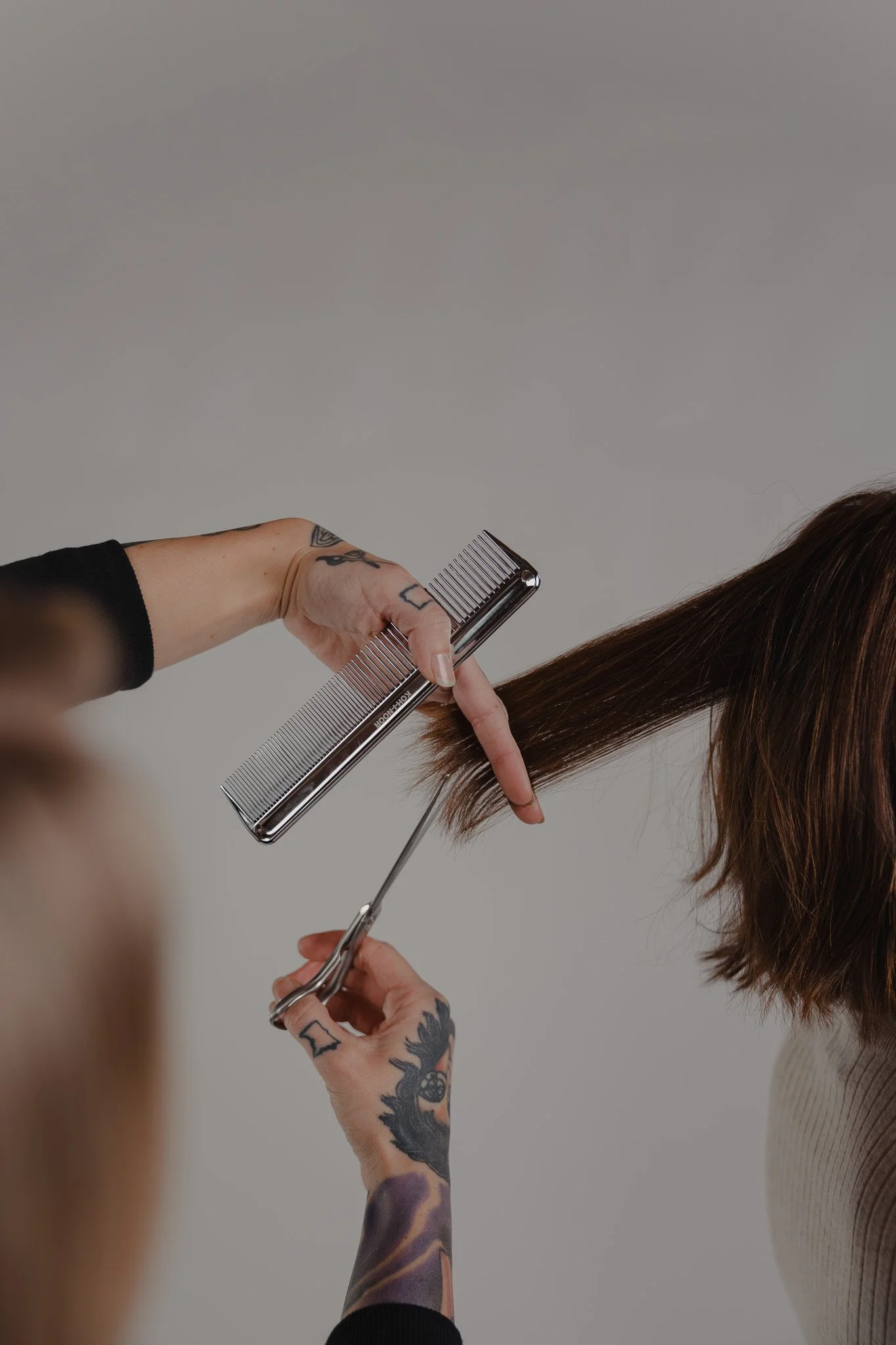 Stylist trimming a client's brown hair with scissors and a comb