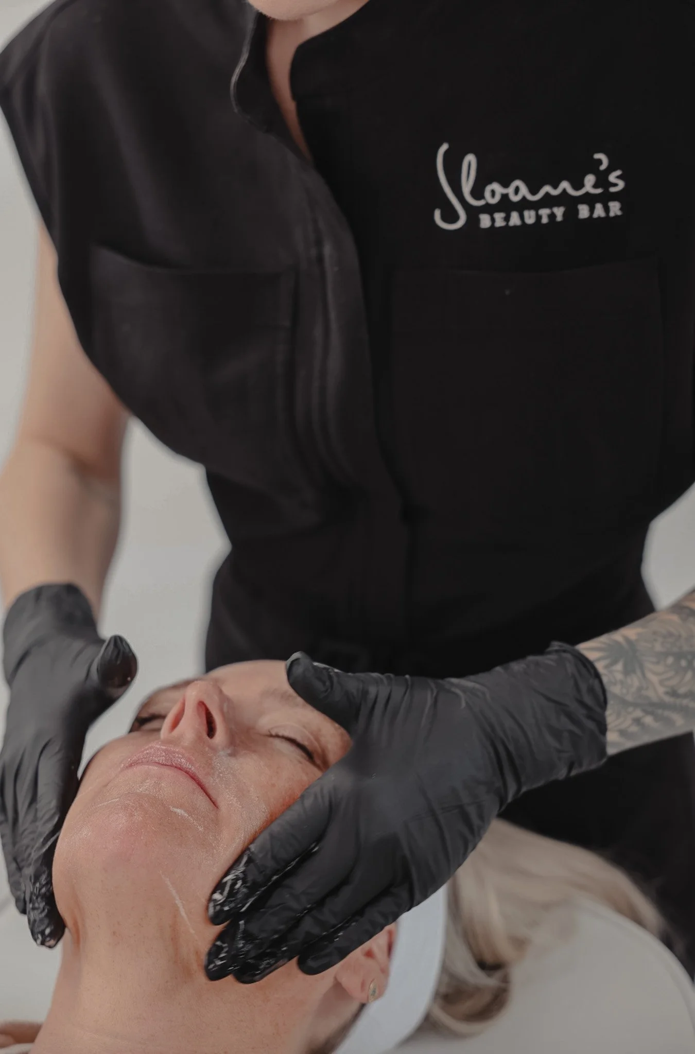 Facial treatment on a client, practitioner wearing Sloane's Beauty Bar shirt