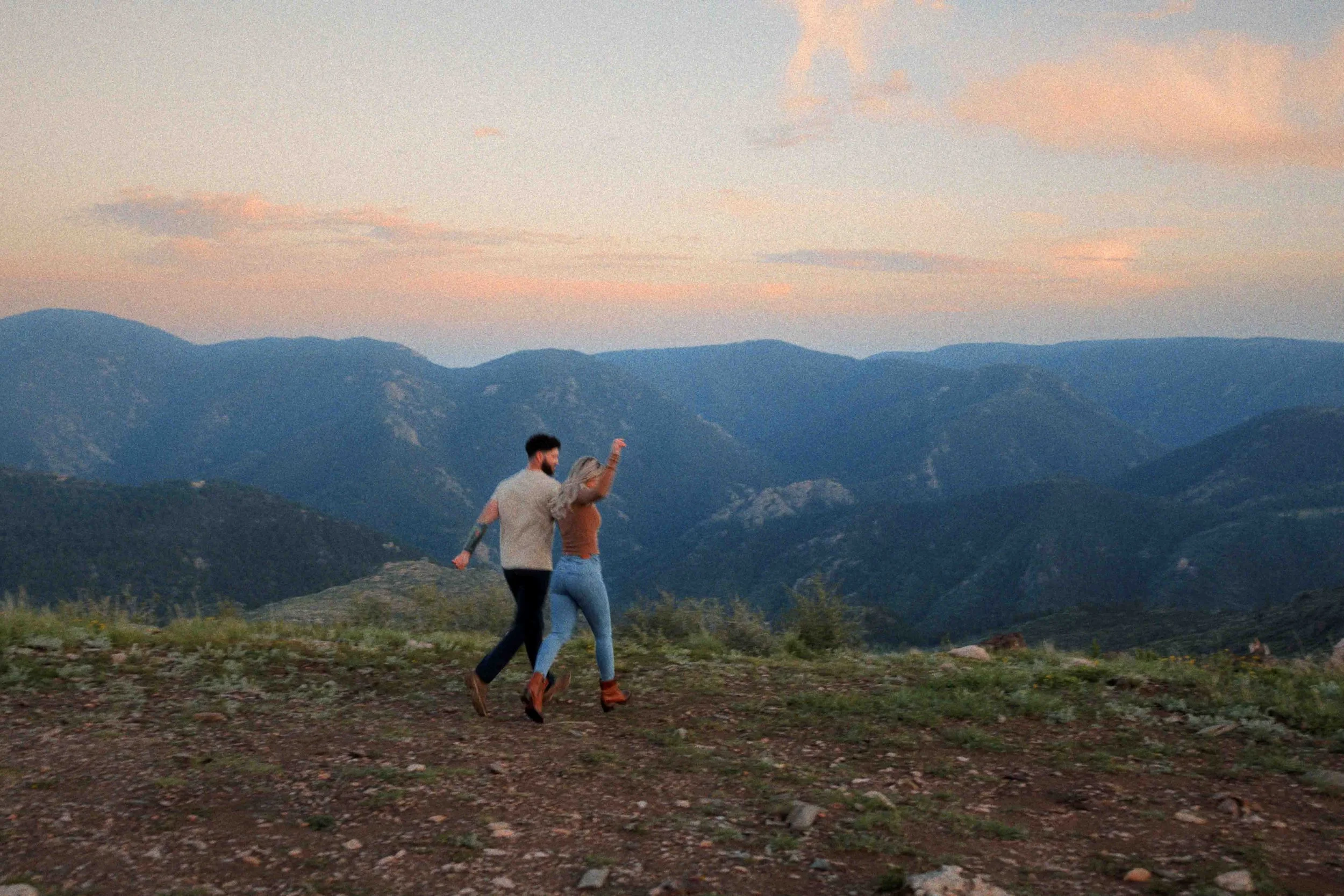 A couple dancing on a mountain landscape during sunset with mountains in the background.