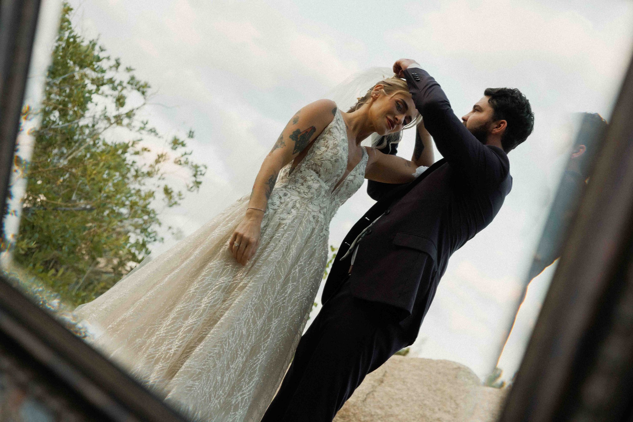Reflection of a bride and groom in a mirror during wedding day, with the groom adjusting the bride's hair and both smiling.
