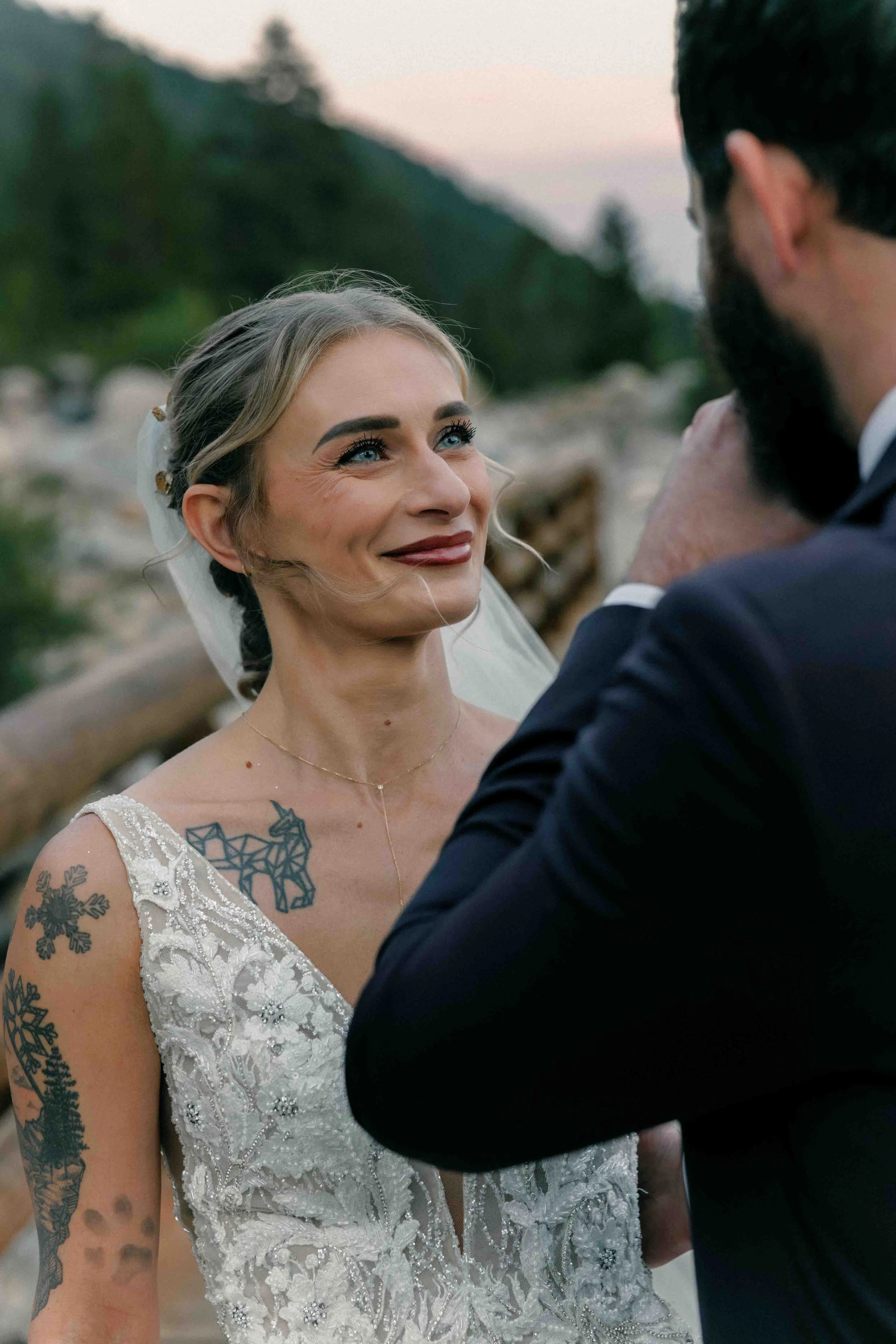Estes Park wedding photographer captures a tattooed bride smiling at her partner during their outdoor mountain ceremony first look.