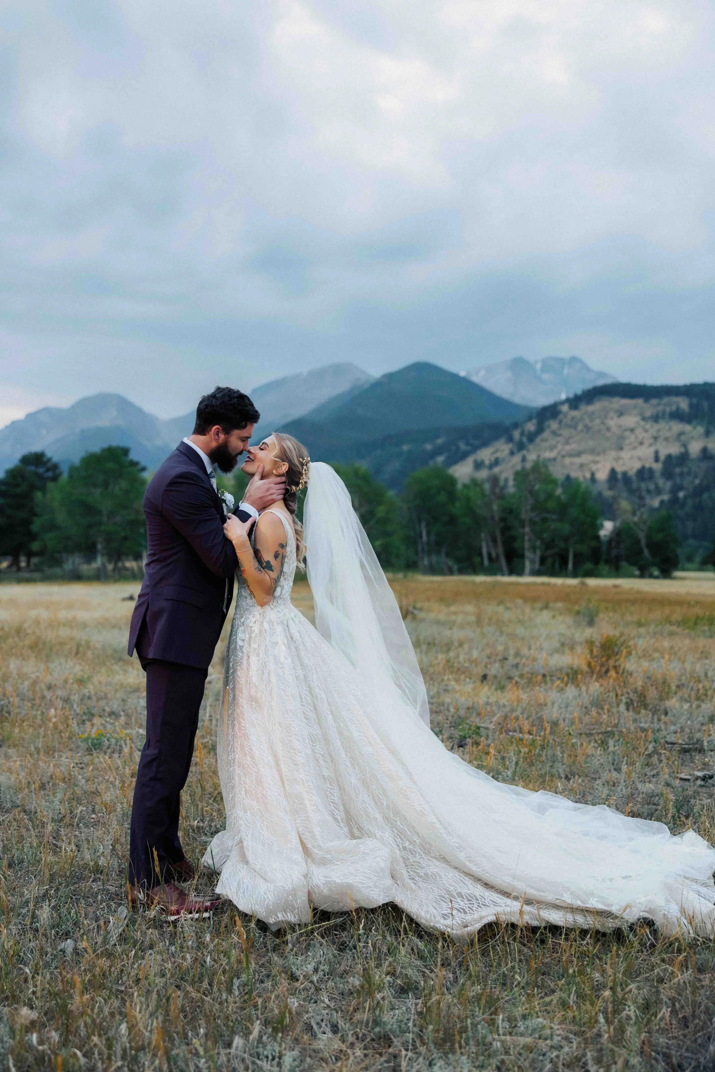 Estes Park wedding photographer captures a bride and groom sharing an intimate moment in a mountain field under cloudy skies.