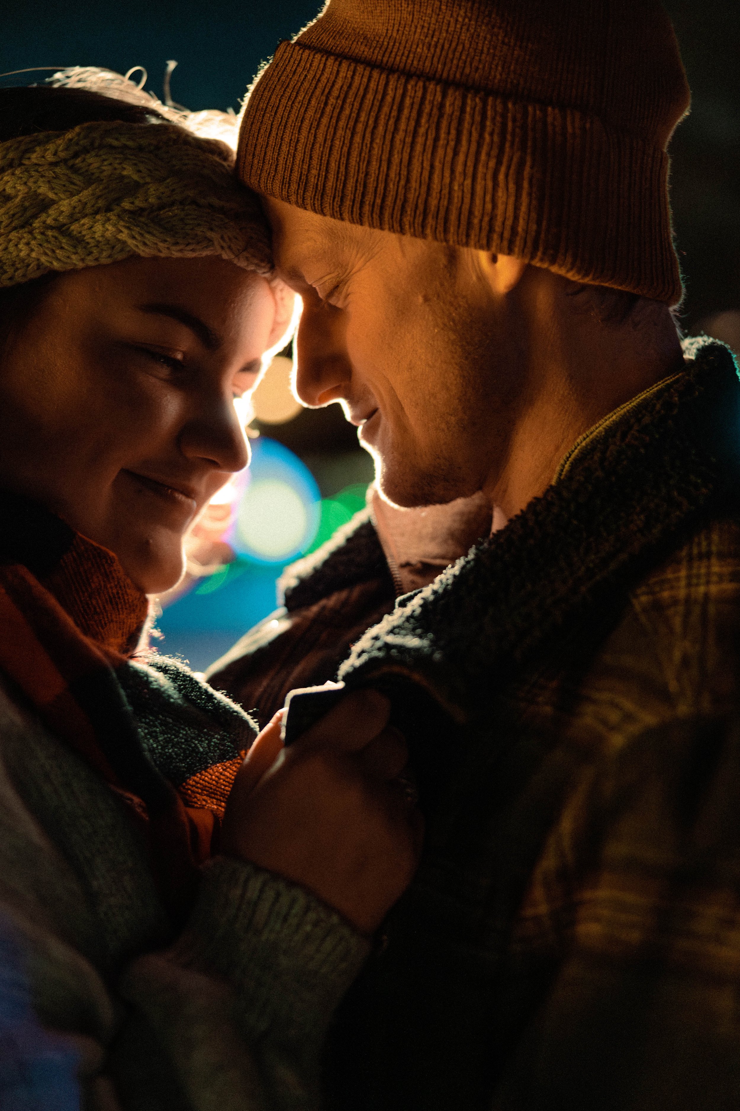 Couple wearing winter clothes, faces close, smiling warmly at each other.