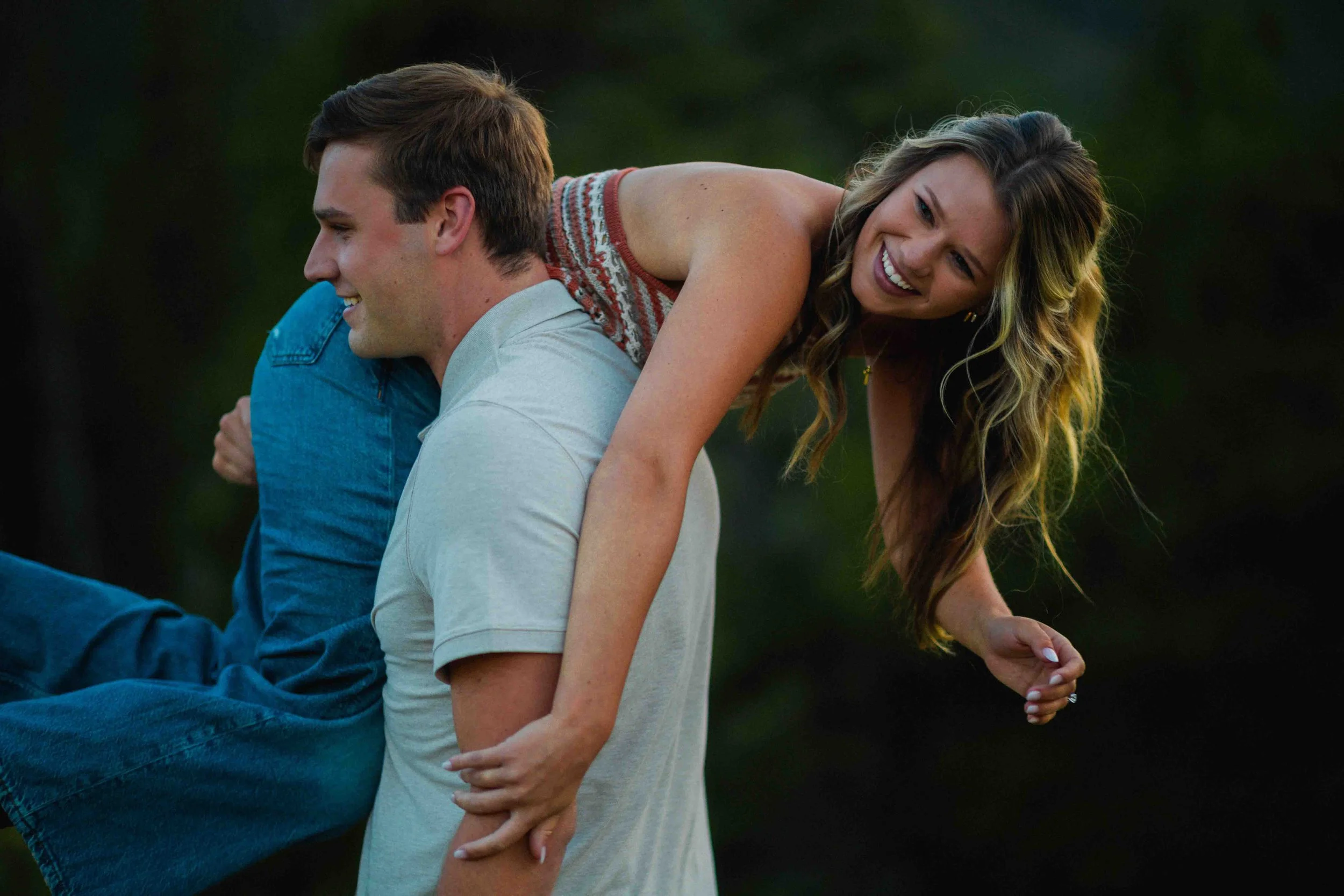 A young couple outdoors, with the woman on the man's back, both smiling and laughing.