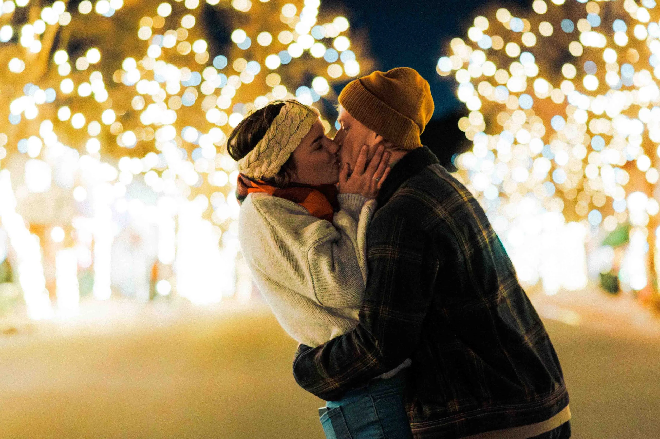 A couple sharing a kiss at night with festive lights in the background