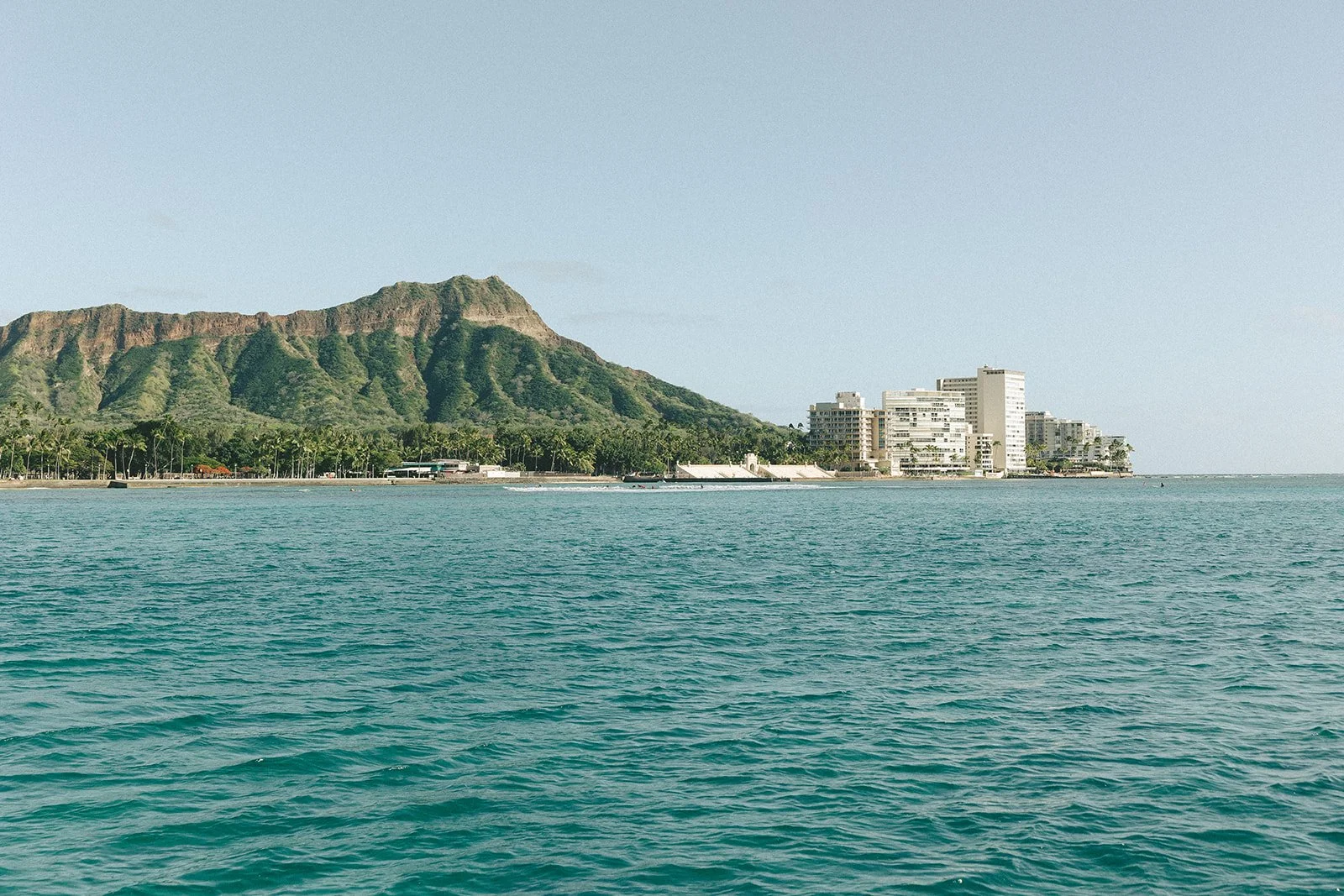 Luxury yacht sailing off the coast of Waikīkī during a vibrant sunset.