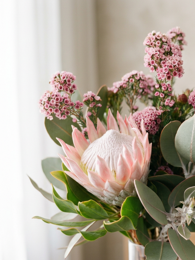 A floral arrangement with a large protea flower surrounded by pink waxflowers and eucalyptus leaves.