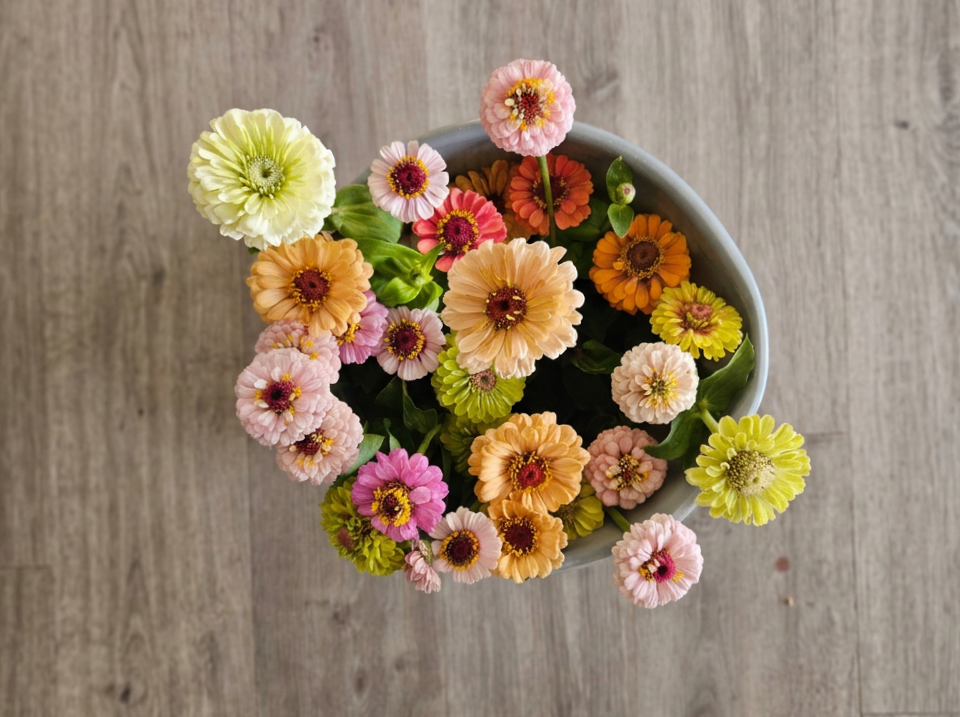 Top-down view of a colorful bouquet of small flowers in a white vase on a wooden surface.