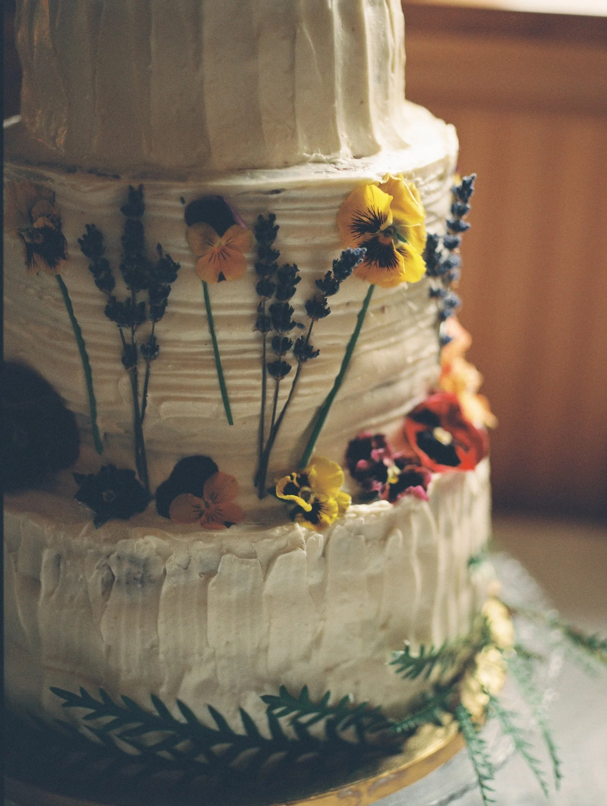 Close-up of a multi-layered wedding cake decorated with edible flowers and greenery.