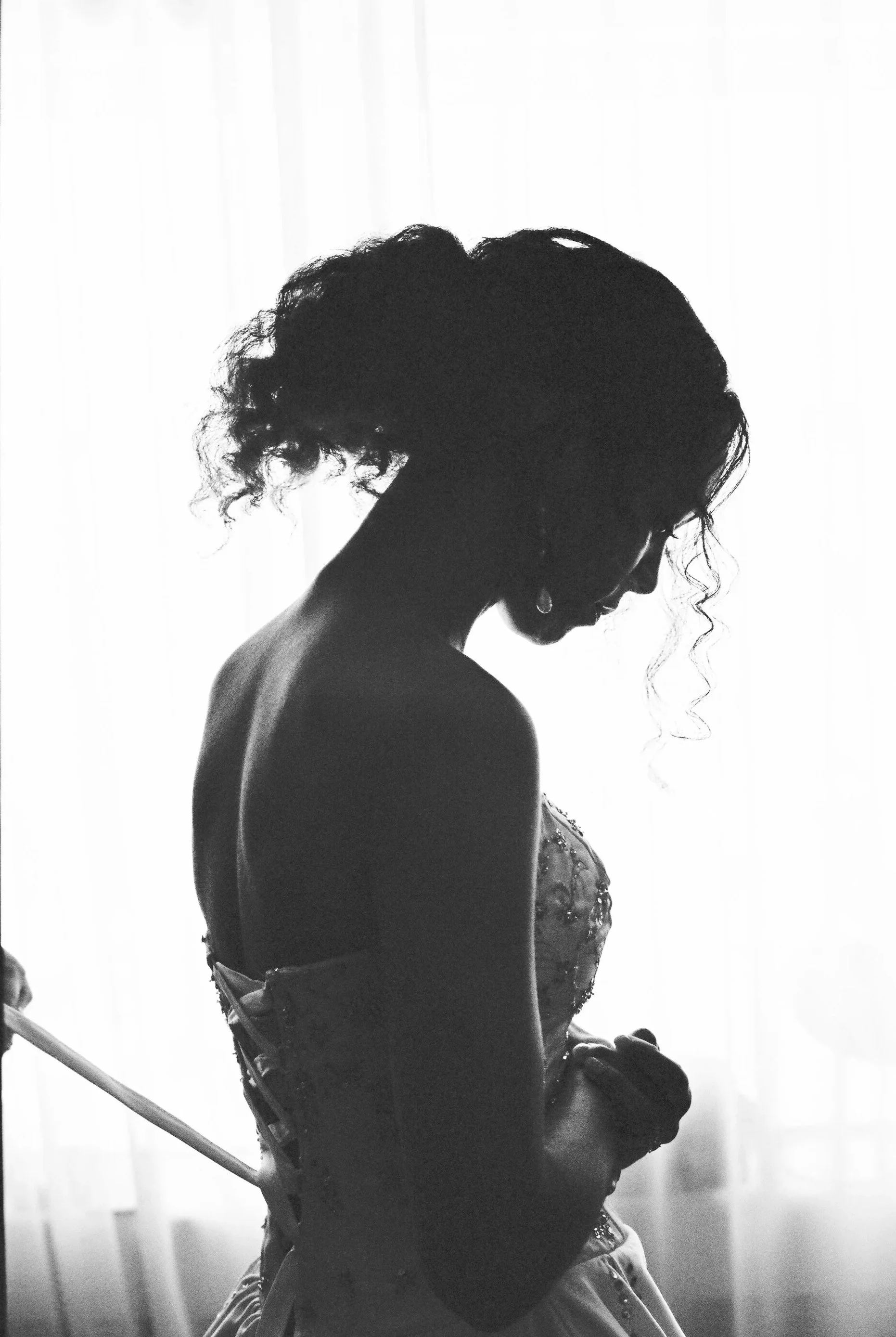Silhouette of a woman with curly hair in a strapless dress, backlit by light from behind, creating a dramatic profile shot.