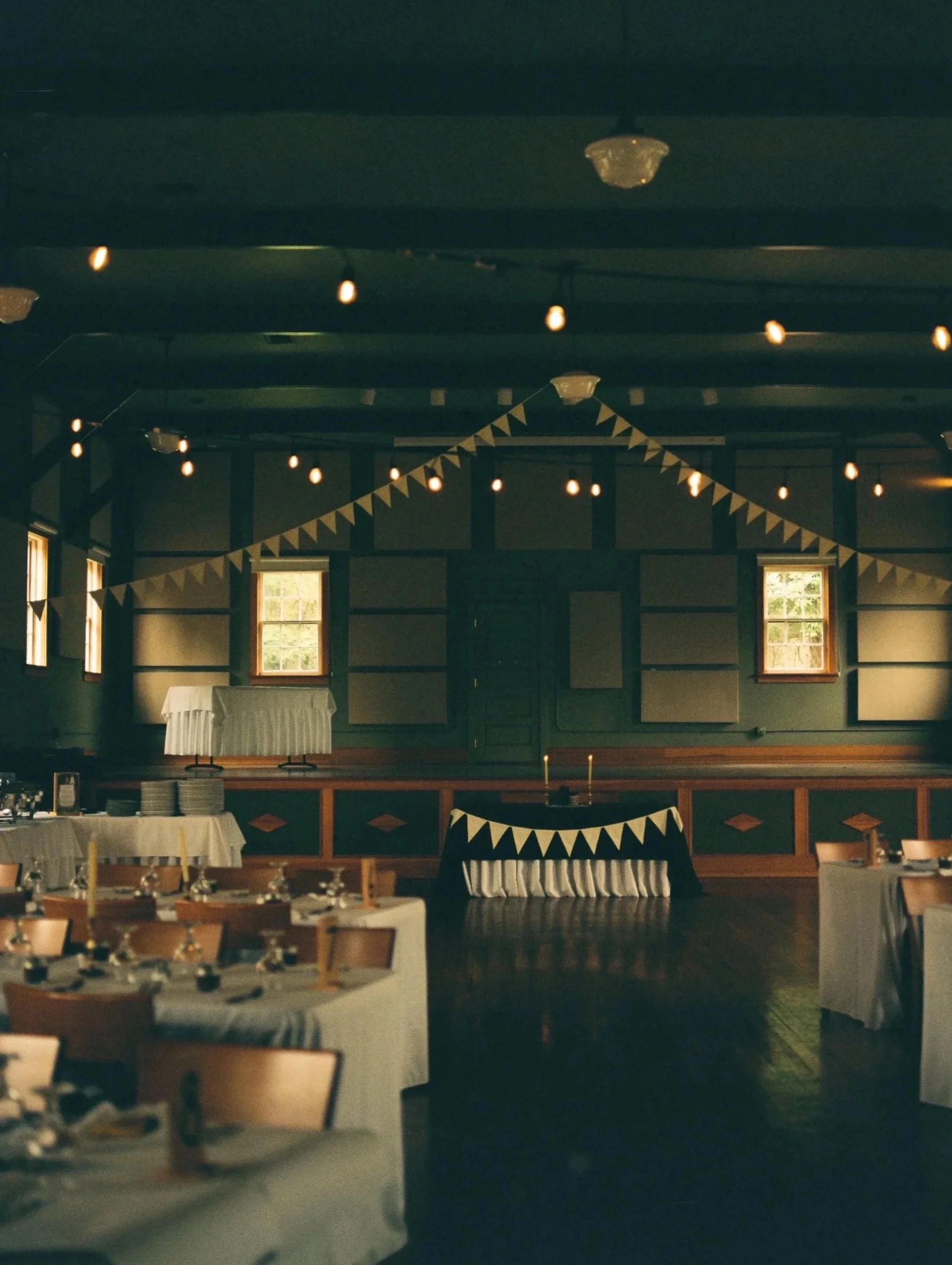 Decorated banquet hall with string lights and bunting, set up for a celebration or event, with tables and chairs arranged for guests.