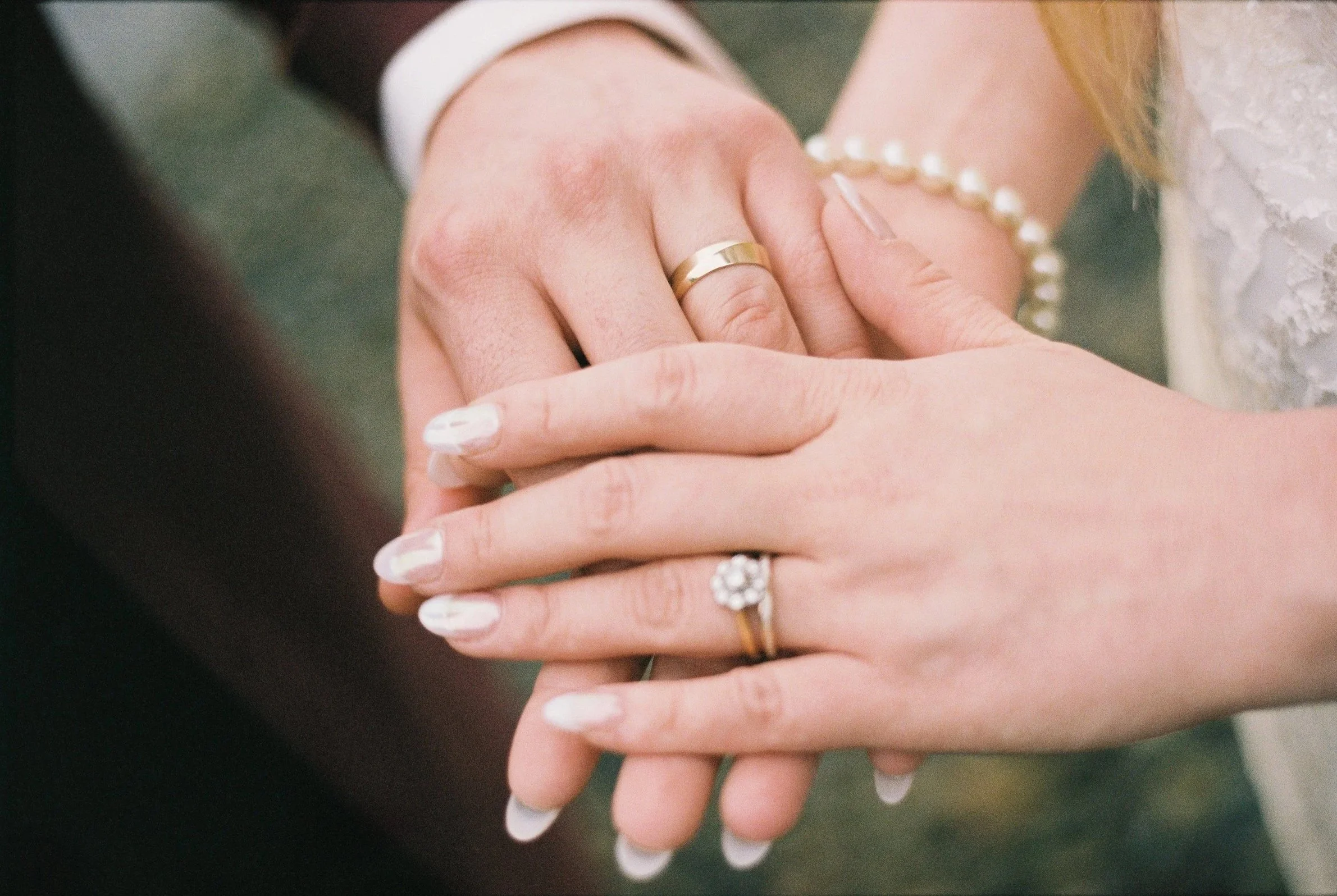 Close-up of a couple holding hands, displaying wedding rings and a pearl bracelet, during a wedding ceremony.