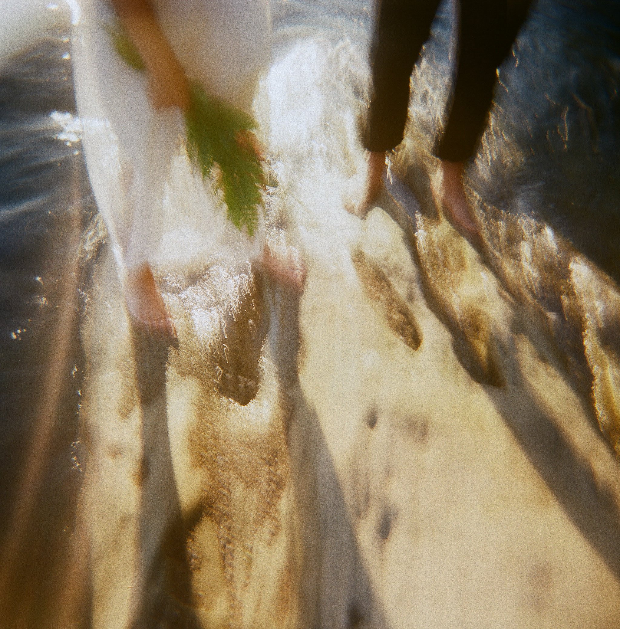 People standing in shallow water at the beach, with waves washing over their feet.