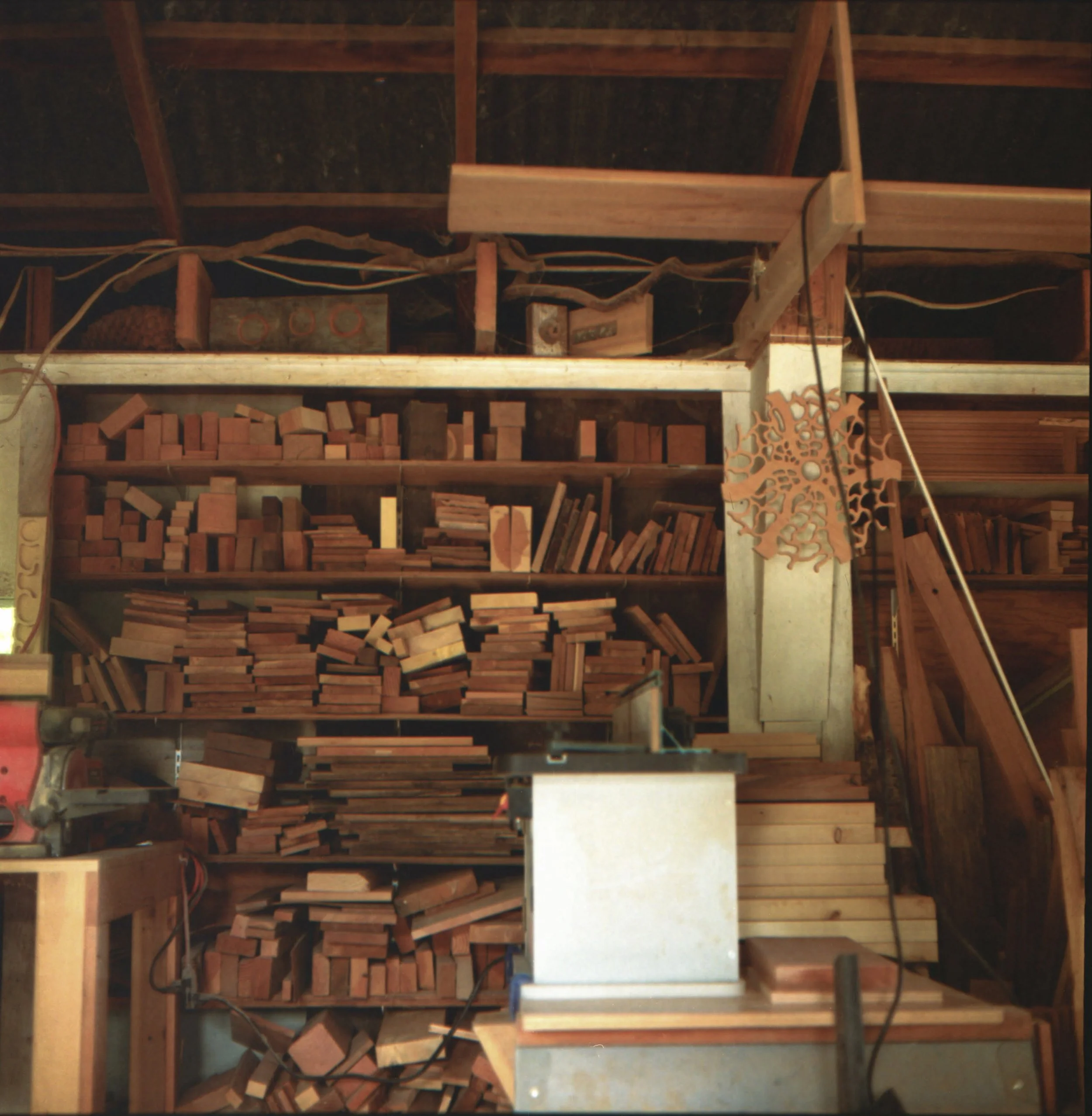 A woodworking shop with shelves filled with various pieces of wood, a workbench, and tools. There is a decorative wooden piece hanging on the wall.