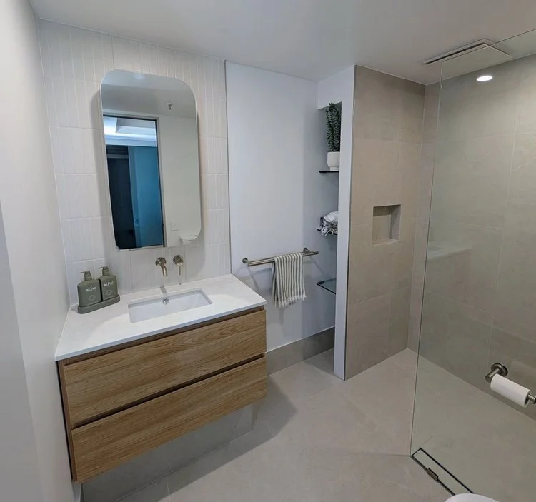 Oak floating vanity with arched mirror and beige tiled walk-in shower — small bathroom renovation Perth 