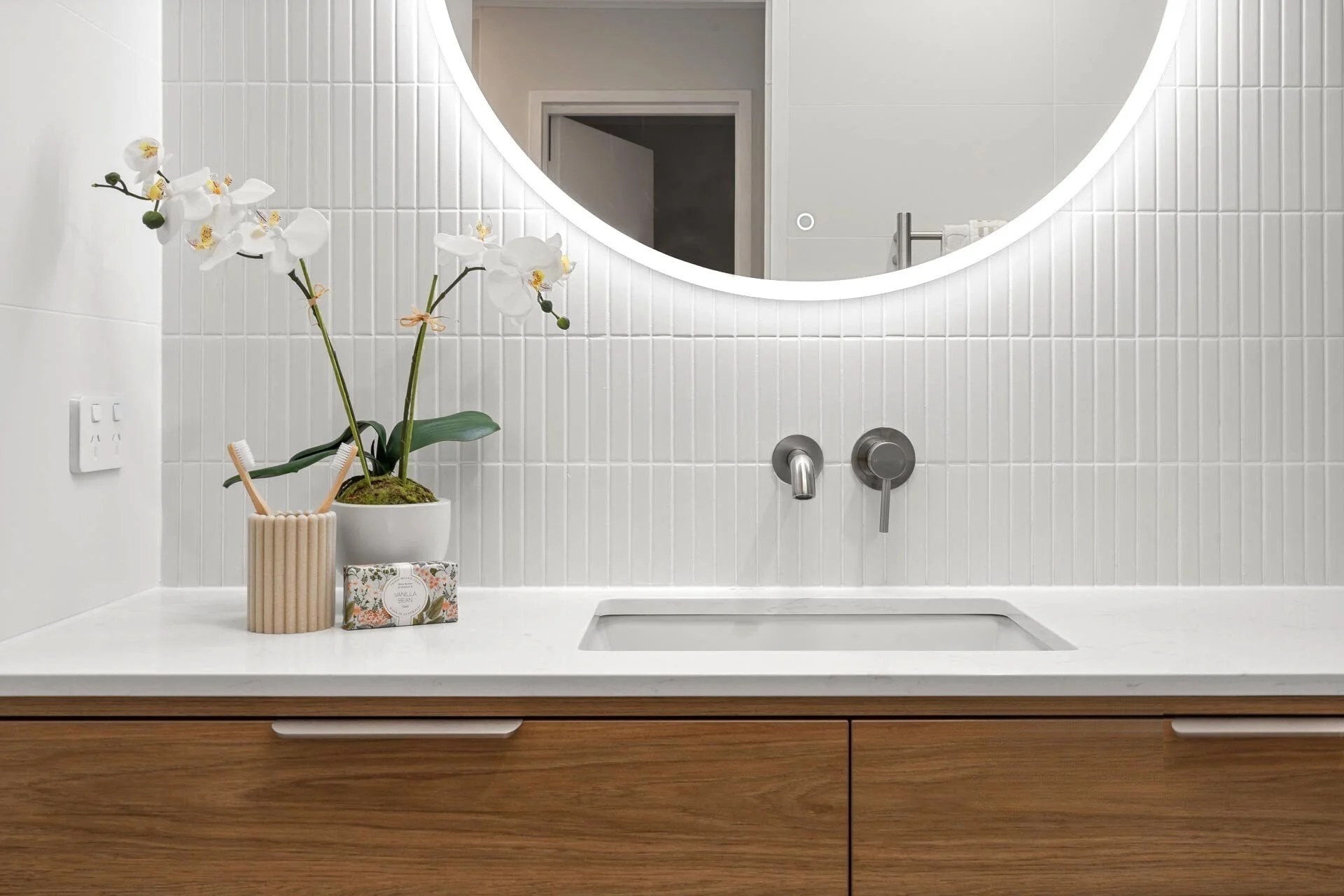Modern bathroom vanity with timber cabinetry, round LED mirror, white tiled splashback and integrated basin in a Mount Lawley bathroom renovation by Renovation Lane WA.