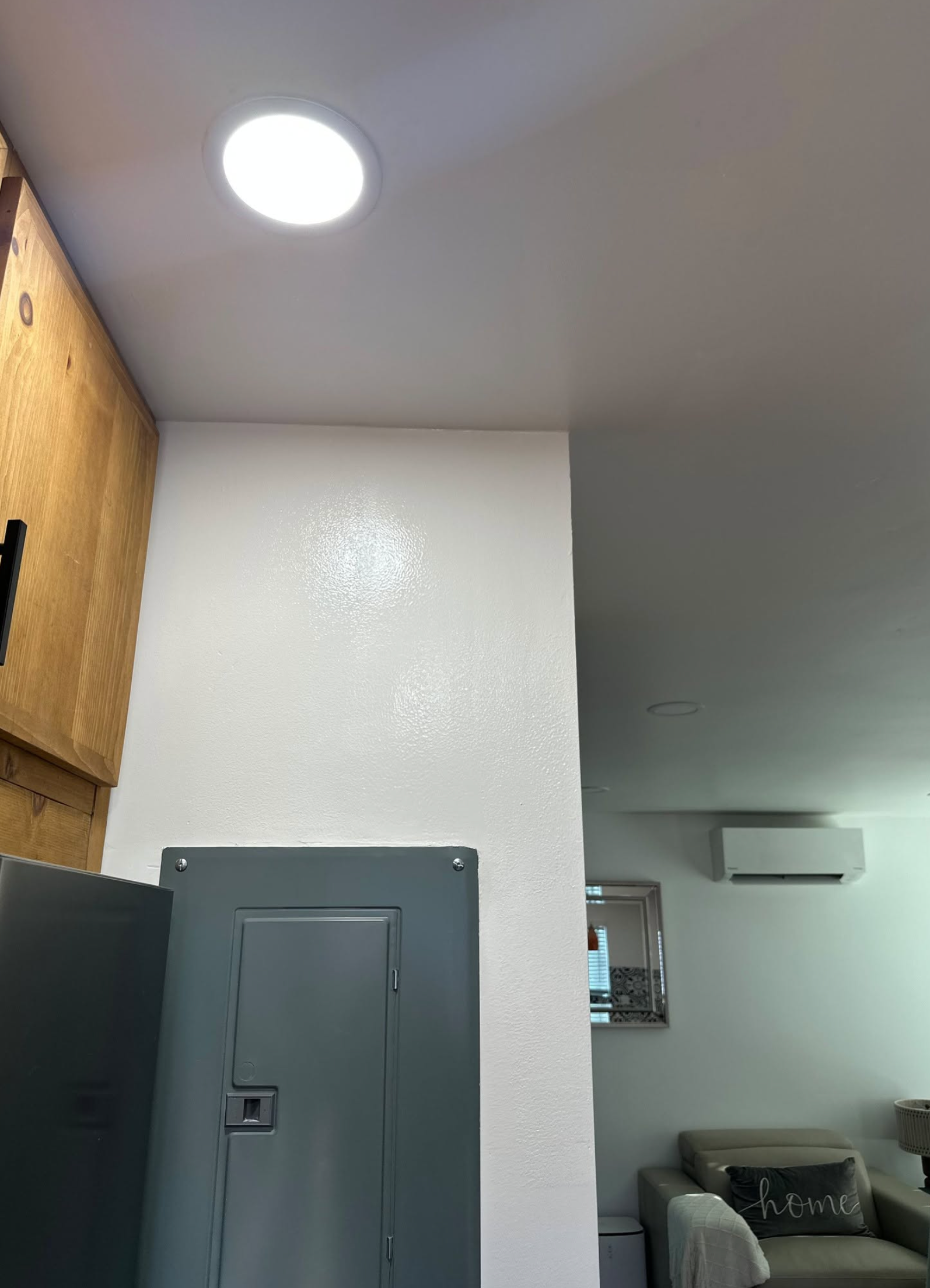 A paint roller with a blue roller sleeve painting a white wall, with a black and white paint sprayer lying on the surface.