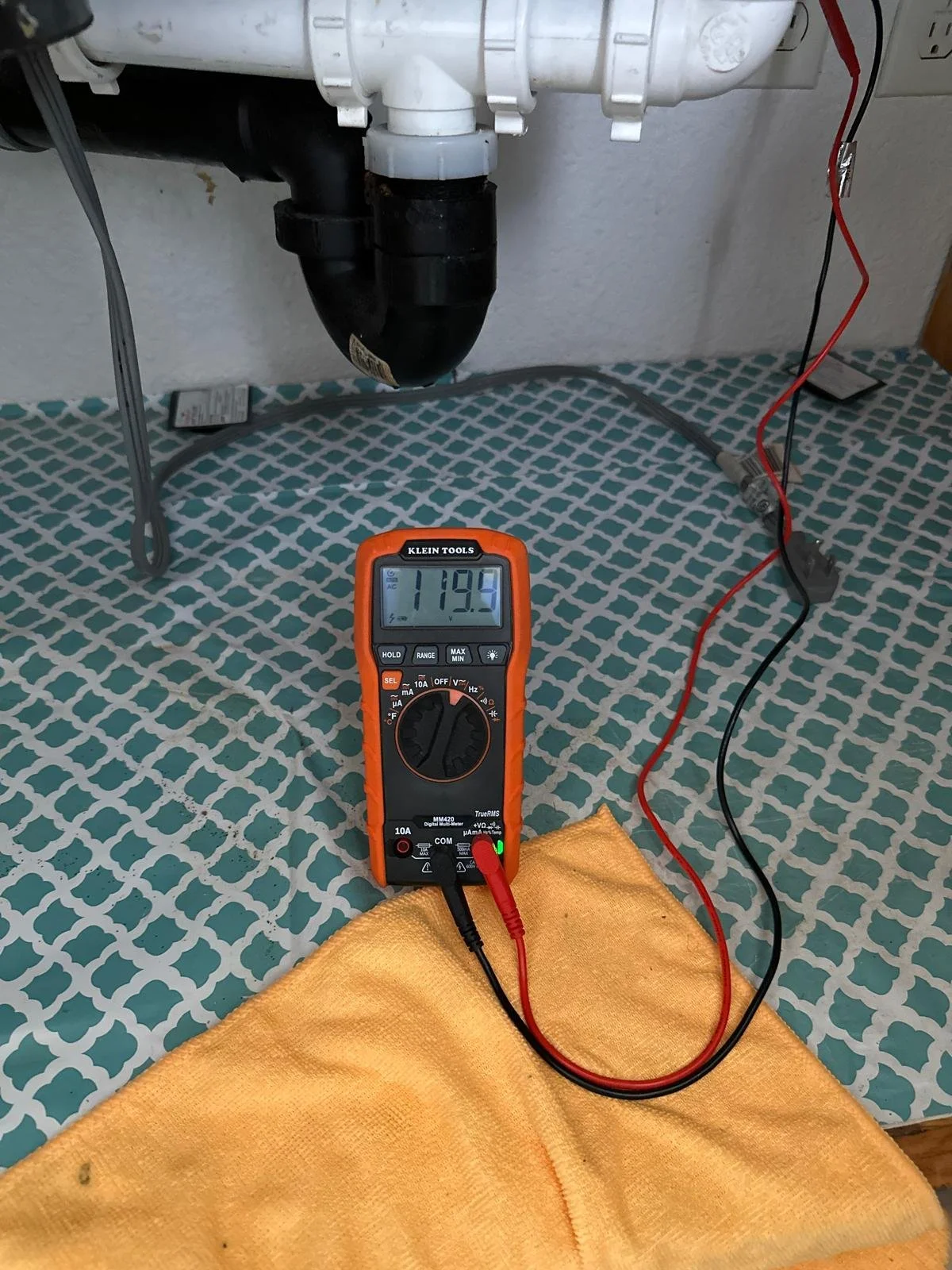 A man wearing a yellow hard hat and yellow work gloves is working on electrical wiring on a wall, using a tool in a non-residential setting.