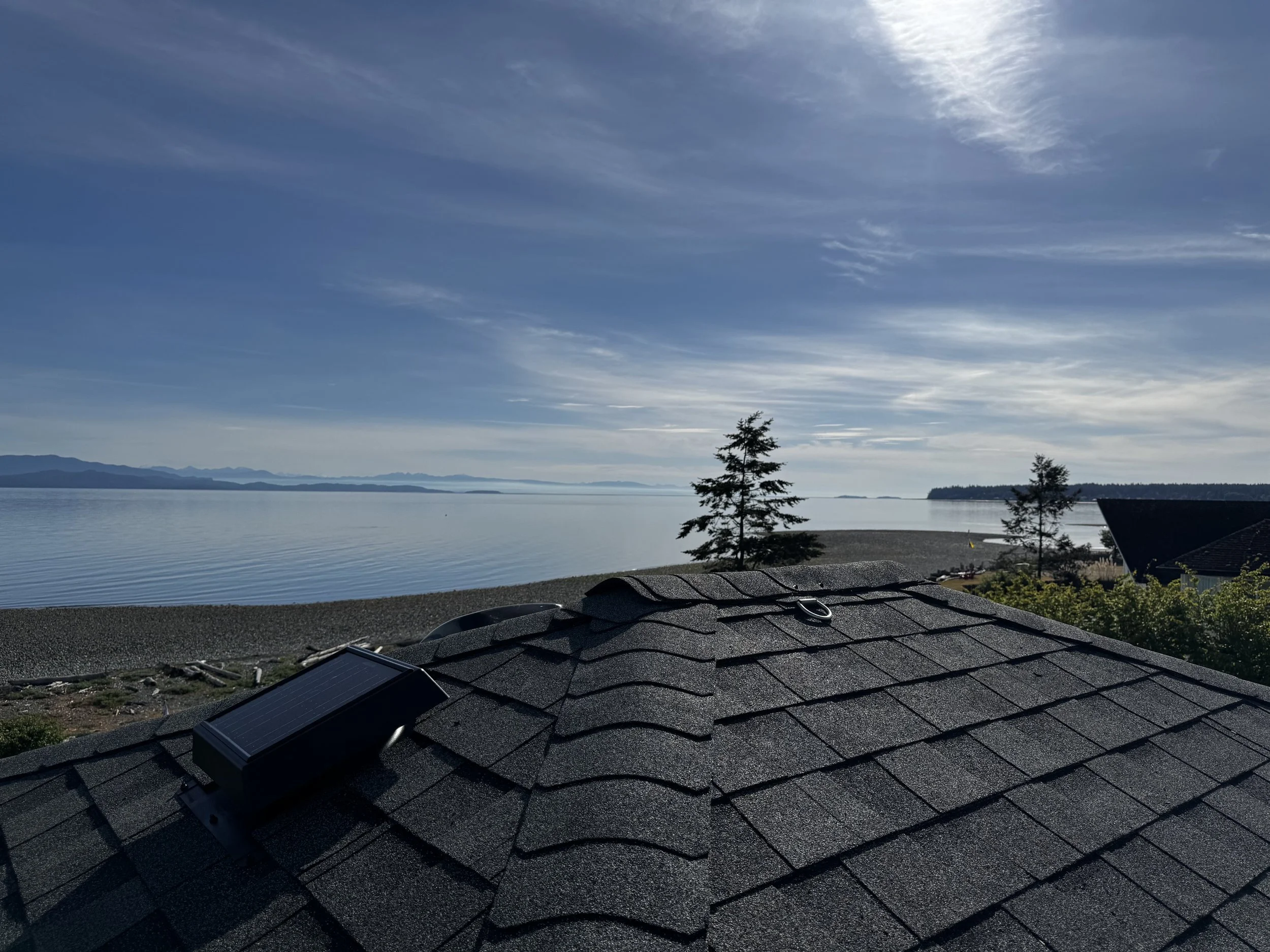 A view of a waterfront landscape with a clear sky, distant mountains, and trees along the shore, viewed from a rooftop with solar panels.