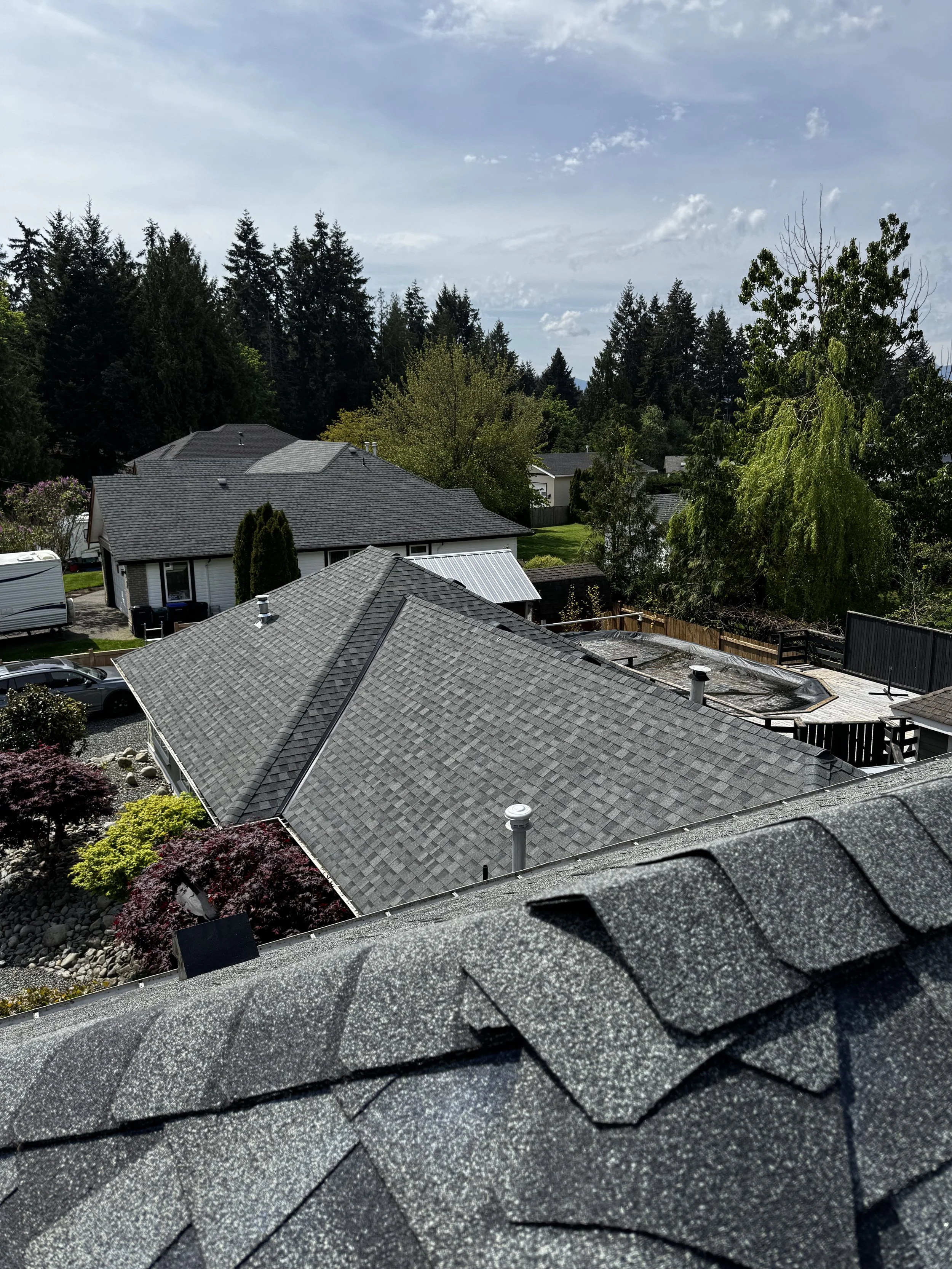 View of rooftops in a suburban neighborhood with trees and a blue sky with clouds.