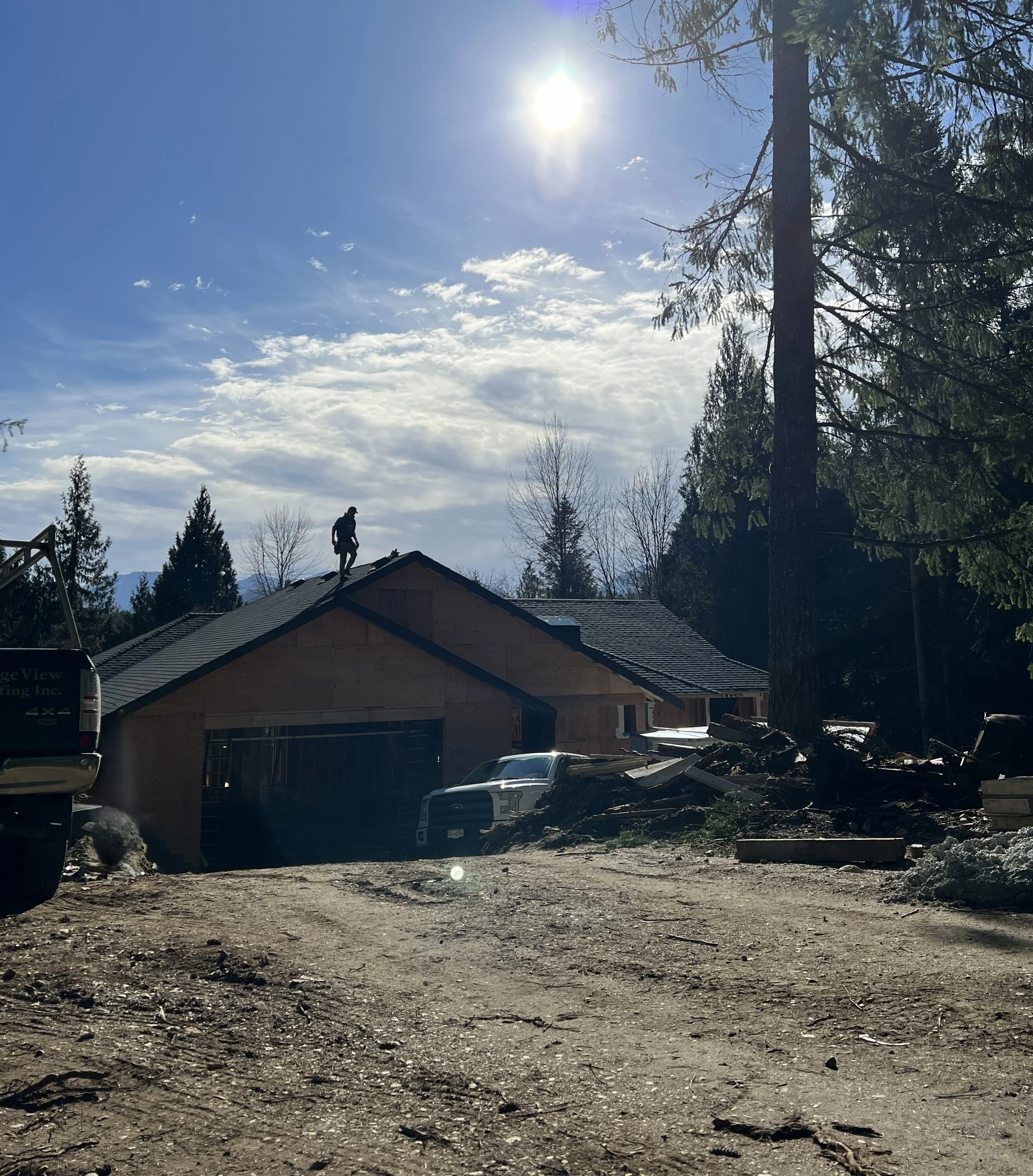 Hilly residential area with houses, vehicles, and trees under a bright sun in a partly cloudy sky, possibly after a storm or wind event.